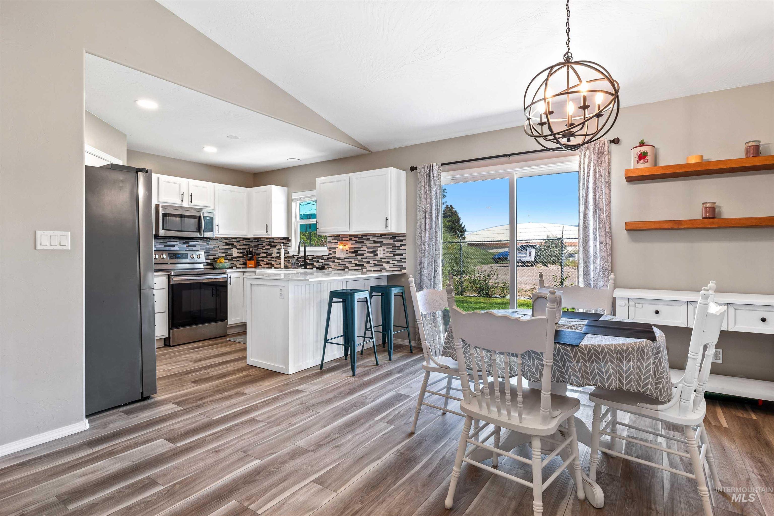 Kitchen with white cabinets, appliances with stainless steel finishes, decorative backsplash, decorative light fixtures, and a breakfast bar