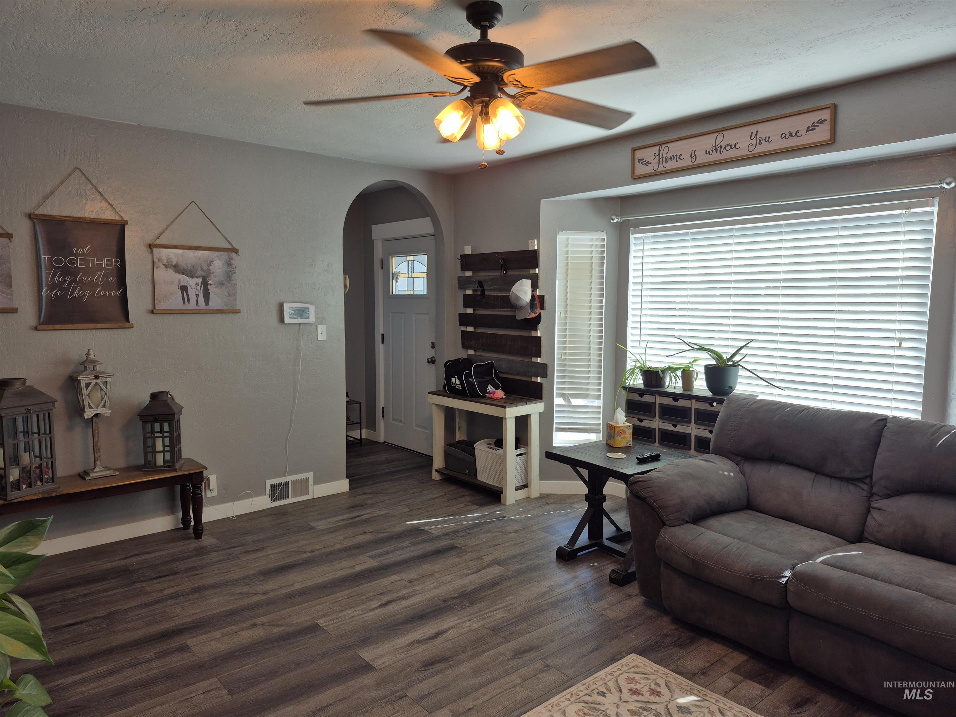 Living area with arched walkways, dark wood-type flooring, a ceiling fan, and a textured ceiling