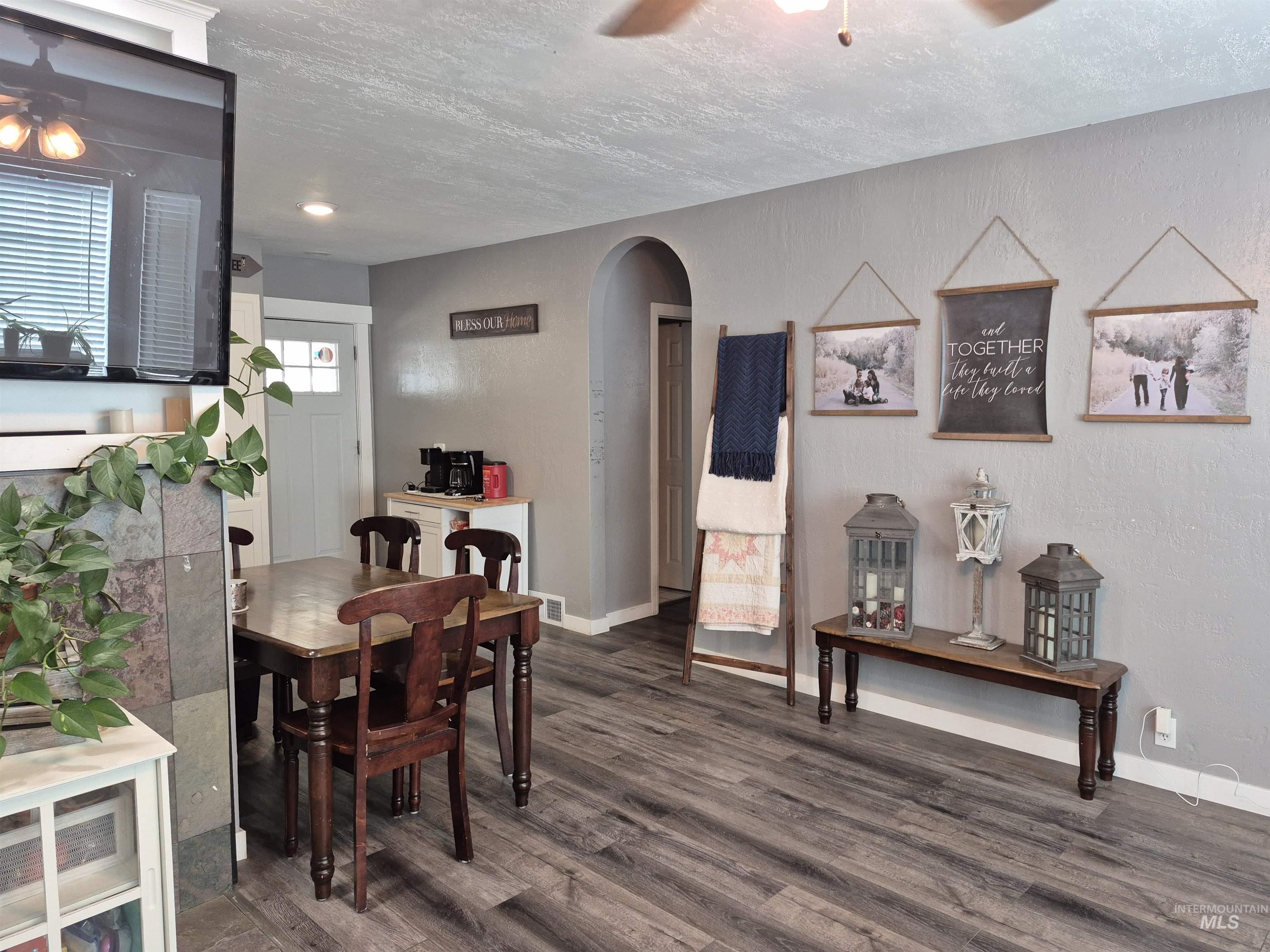 Dining area featuring a ceiling fan, a textured ceiling, dark wood-style floors, arched walkways, and a textured wall