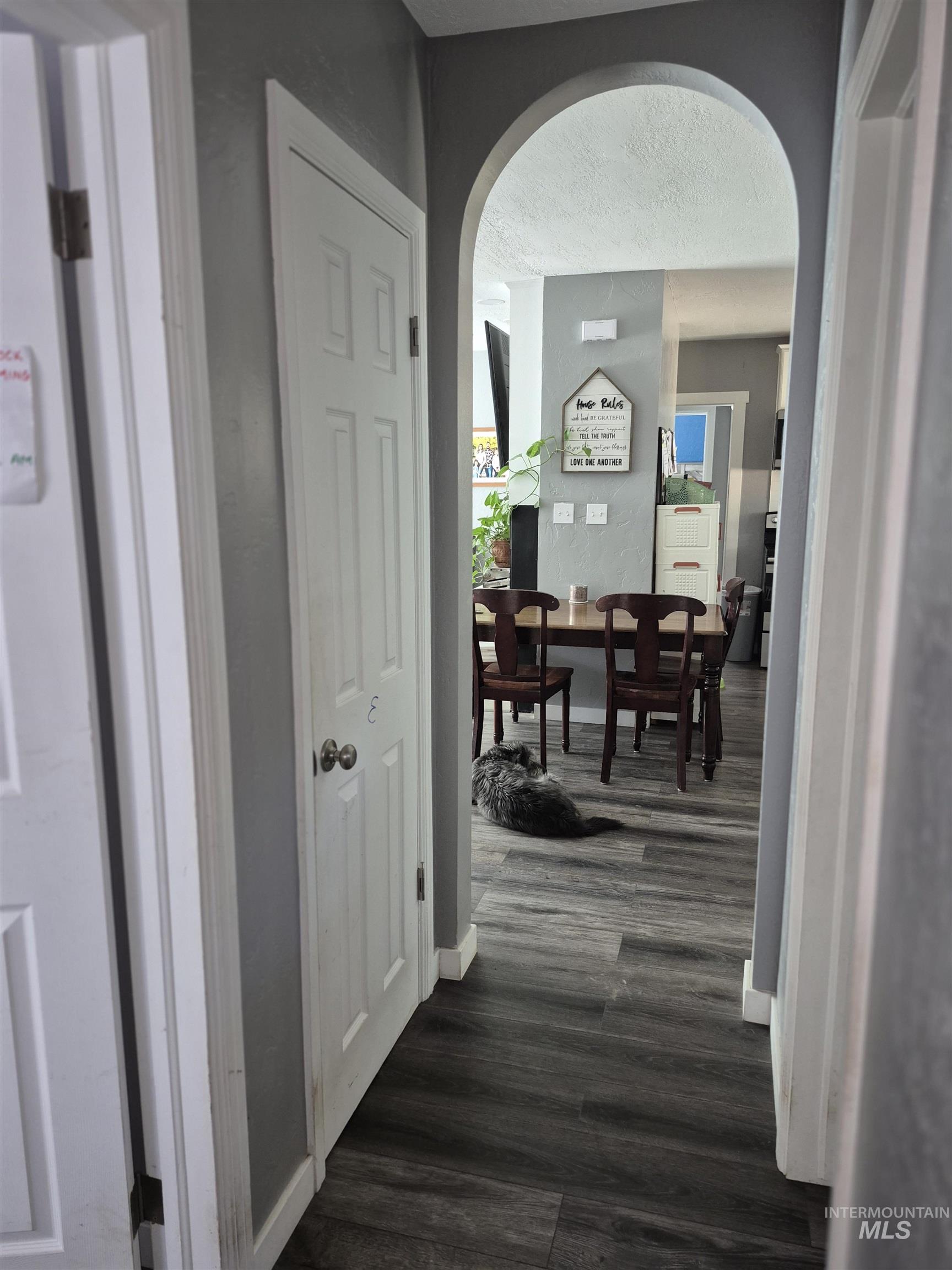 Hallway with dark wood-type flooring, arched walkways, and a textured ceiling