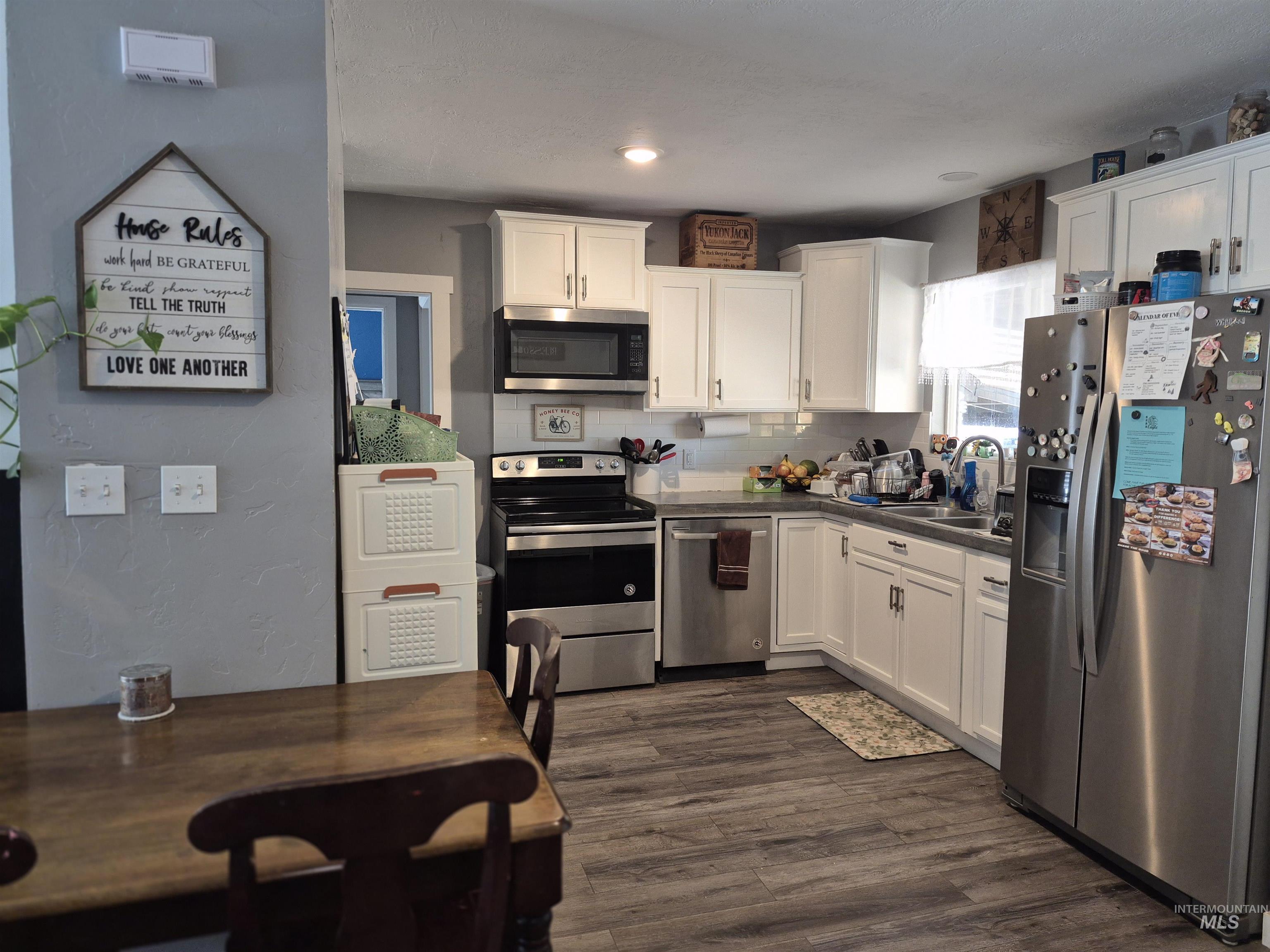 Kitchen featuring appliances with stainless steel finishes, white cabinetry, decorative backsplash, dark wood-type flooring, and a textured wall