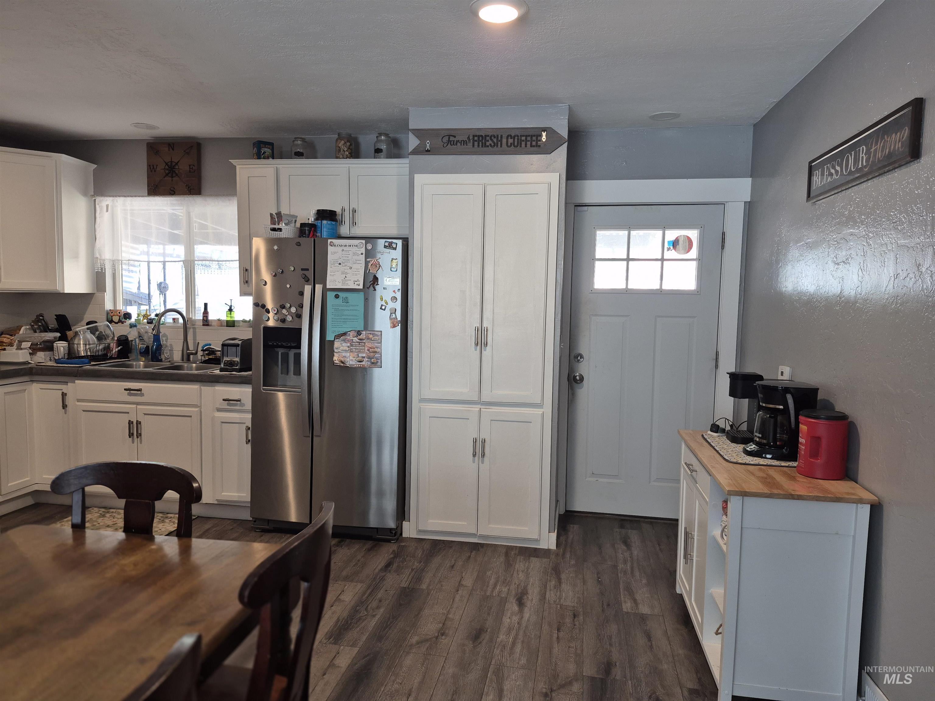 Kitchen with stainless steel fridge, white cabinets, dark wood-style flooring, and a textured wall