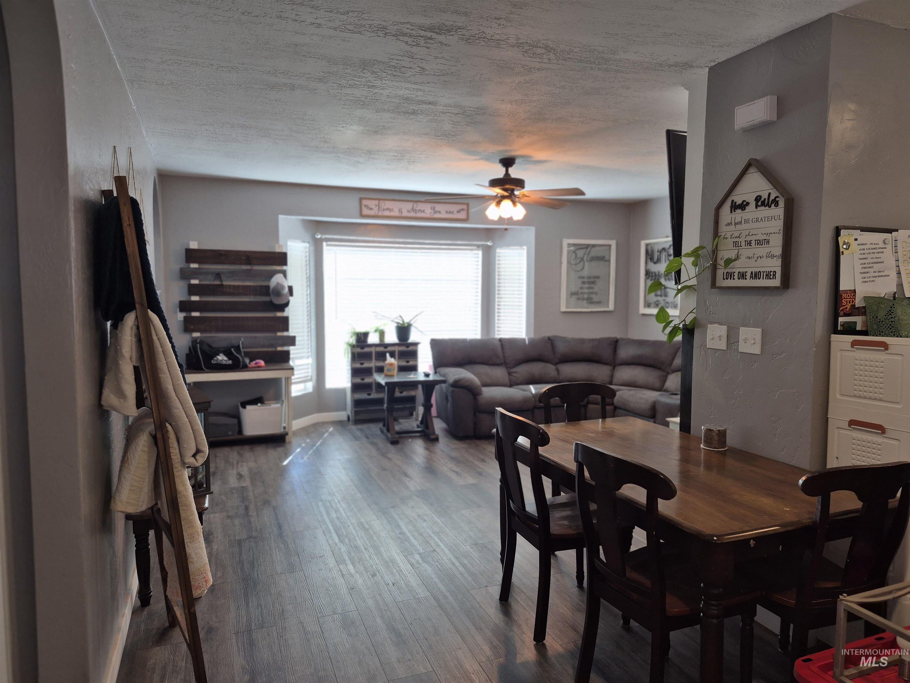 Dining space featuring dark wood-type flooring, a textured ceiling, a ceiling fan, and a textured wall