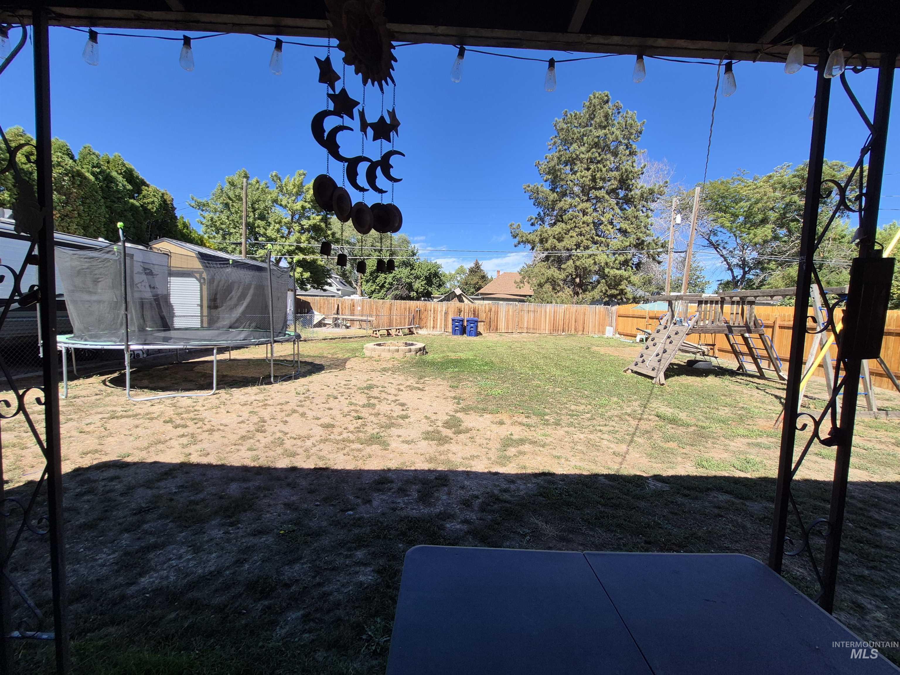 Fenced backyard with a trampoline, a playground, and a patio area