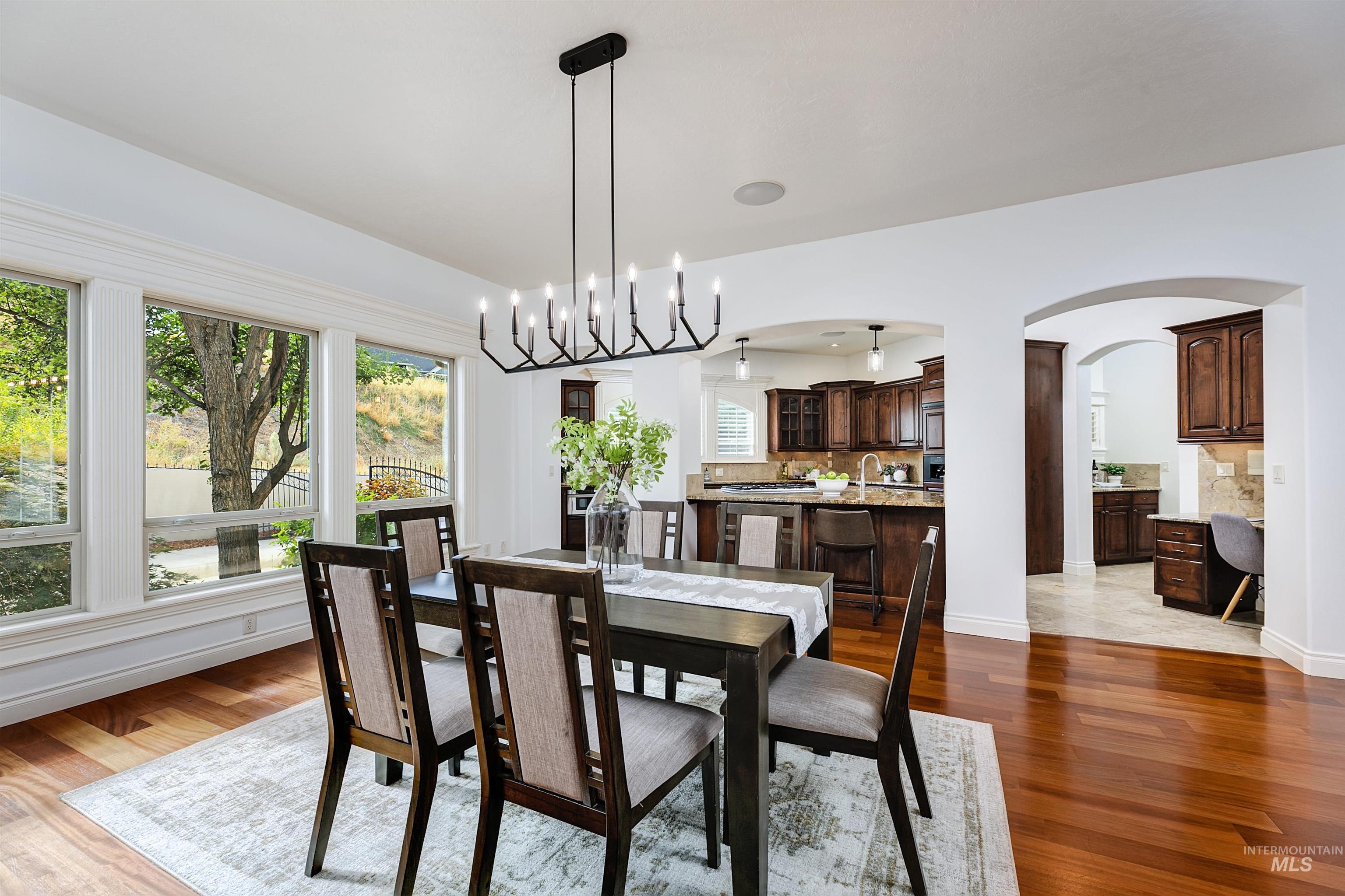 Dining area with arched walkways, a chandelier, healthy amount of natural light, and dark wood finished floors