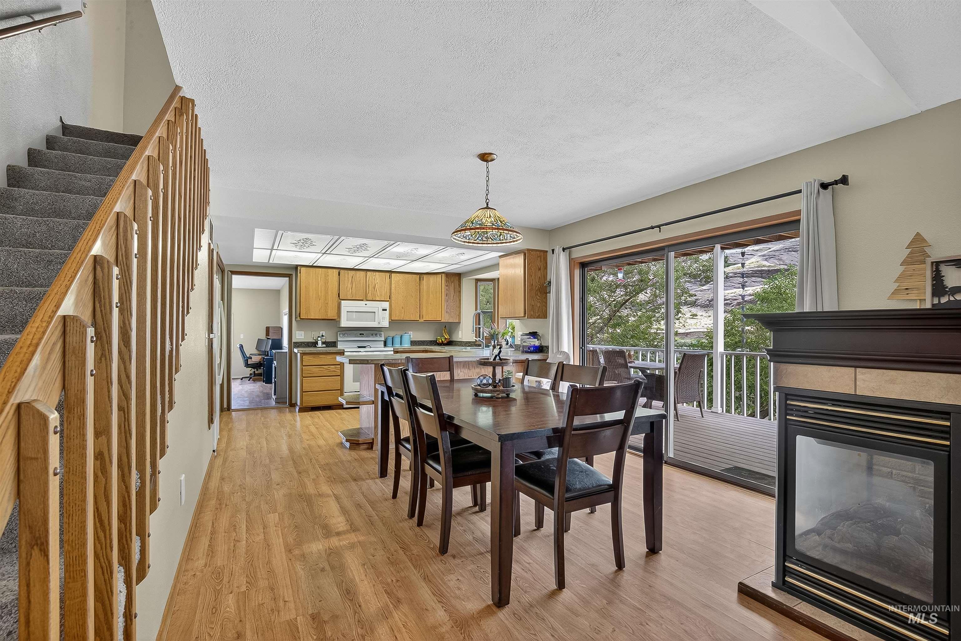 Dining area with light wood finished floors, stairway, a multi sided fireplace, and a textured ceiling