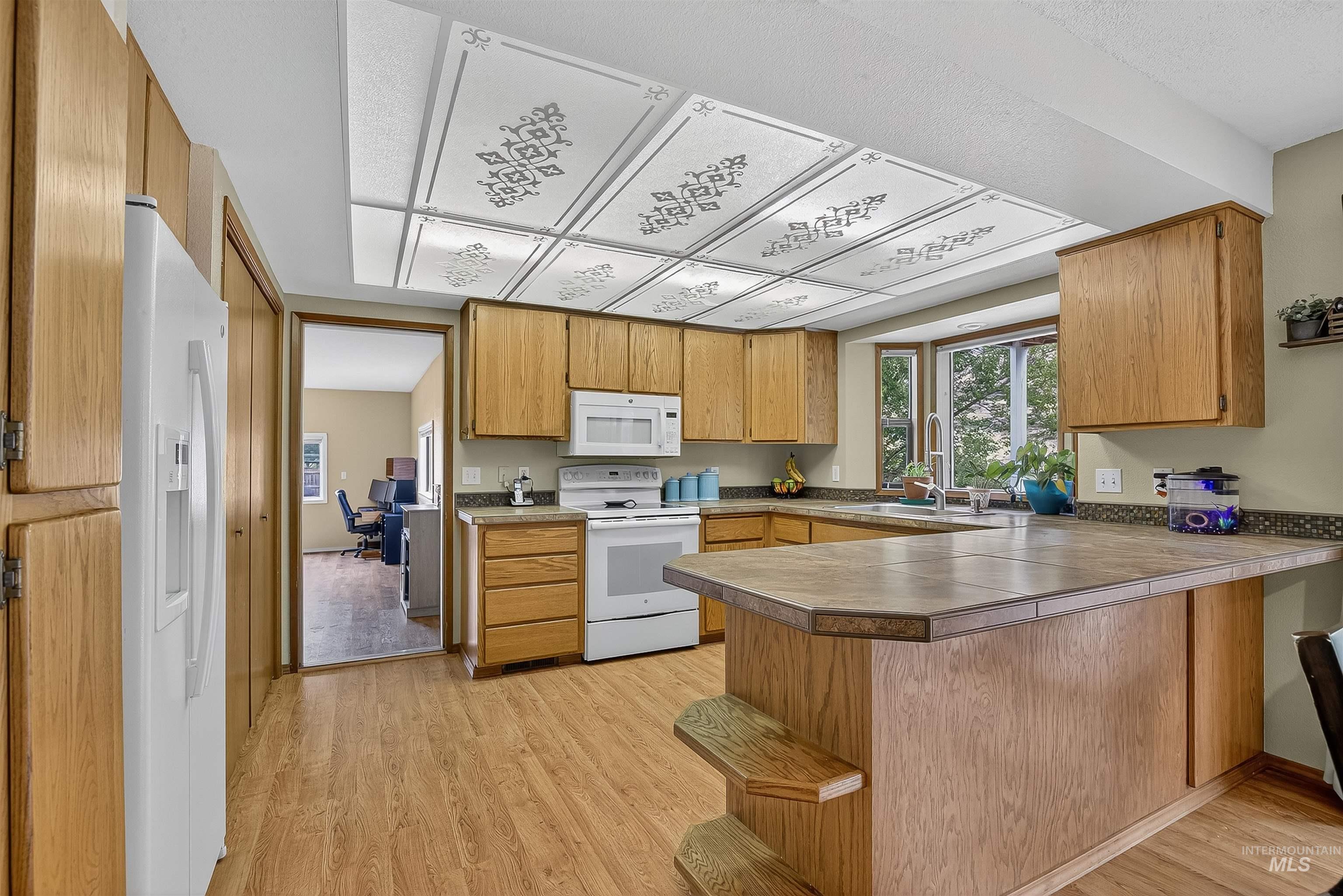 Kitchen featuring a peninsula, white appliances, light wood-style flooring, brown cabinets, and light countertops