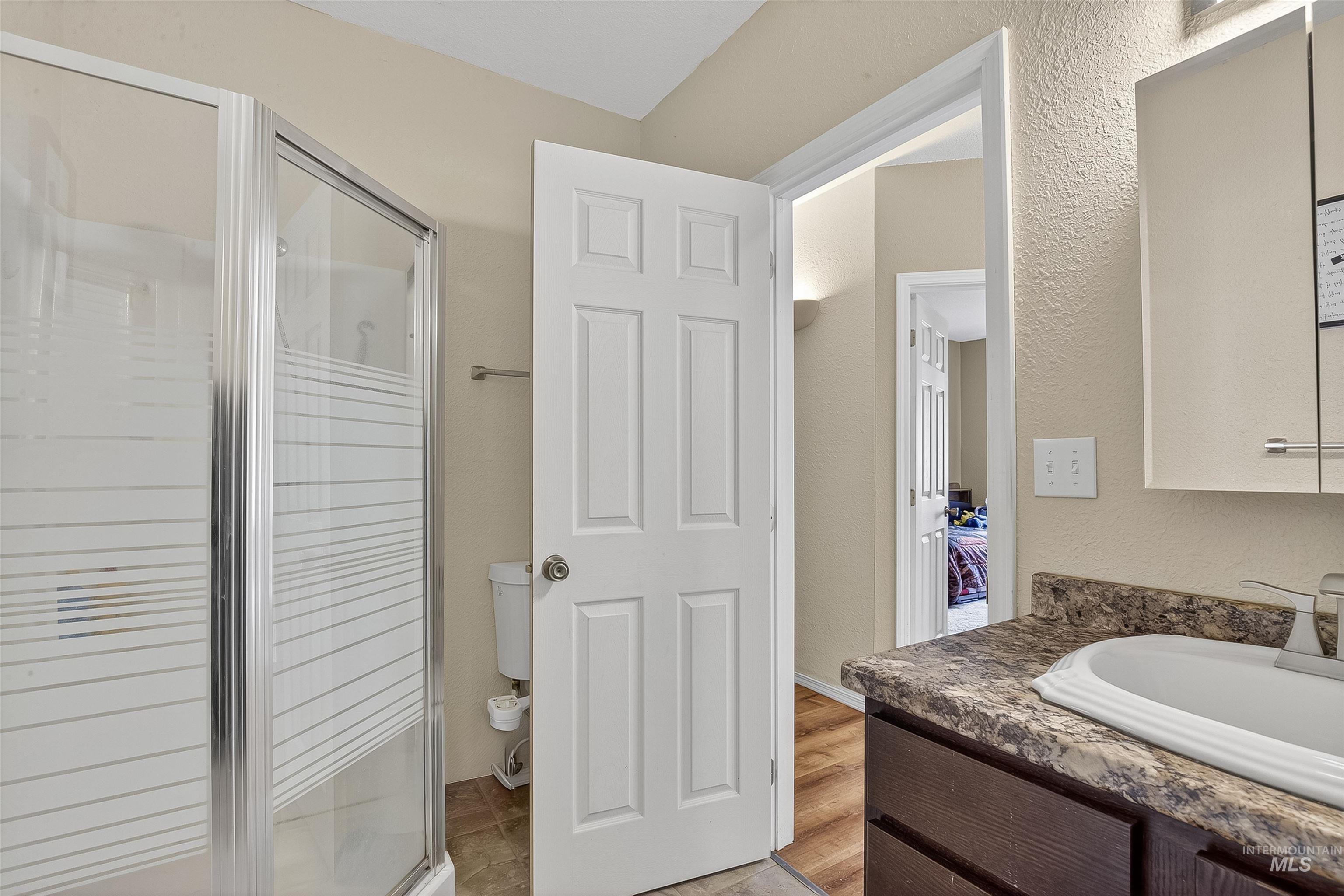 Bathroom with vanity, a textured wall, a stall shower, and light wood-type flooring