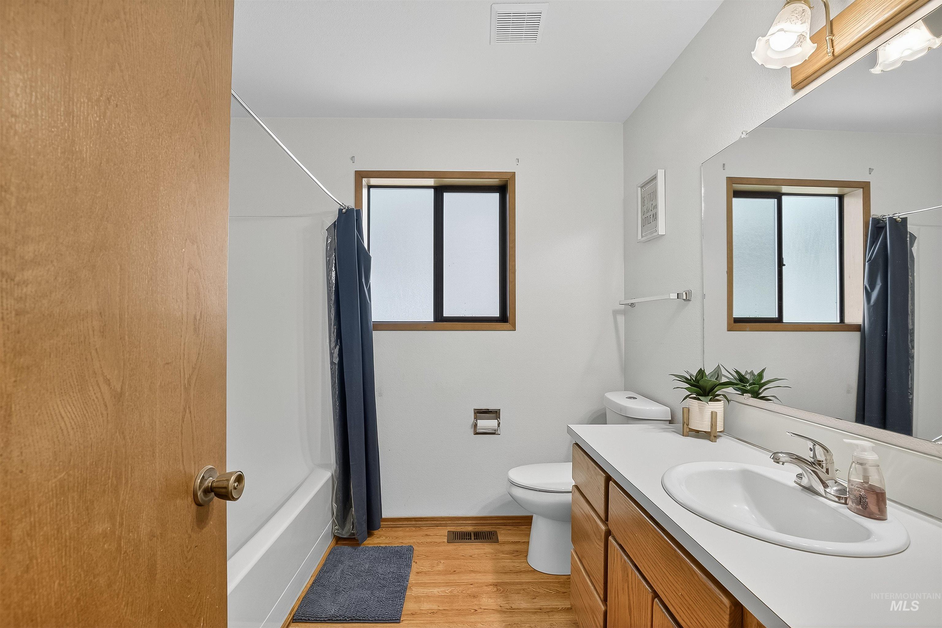 Full bath with light wood-style flooring, shower / bath combination with curtain, and vanity