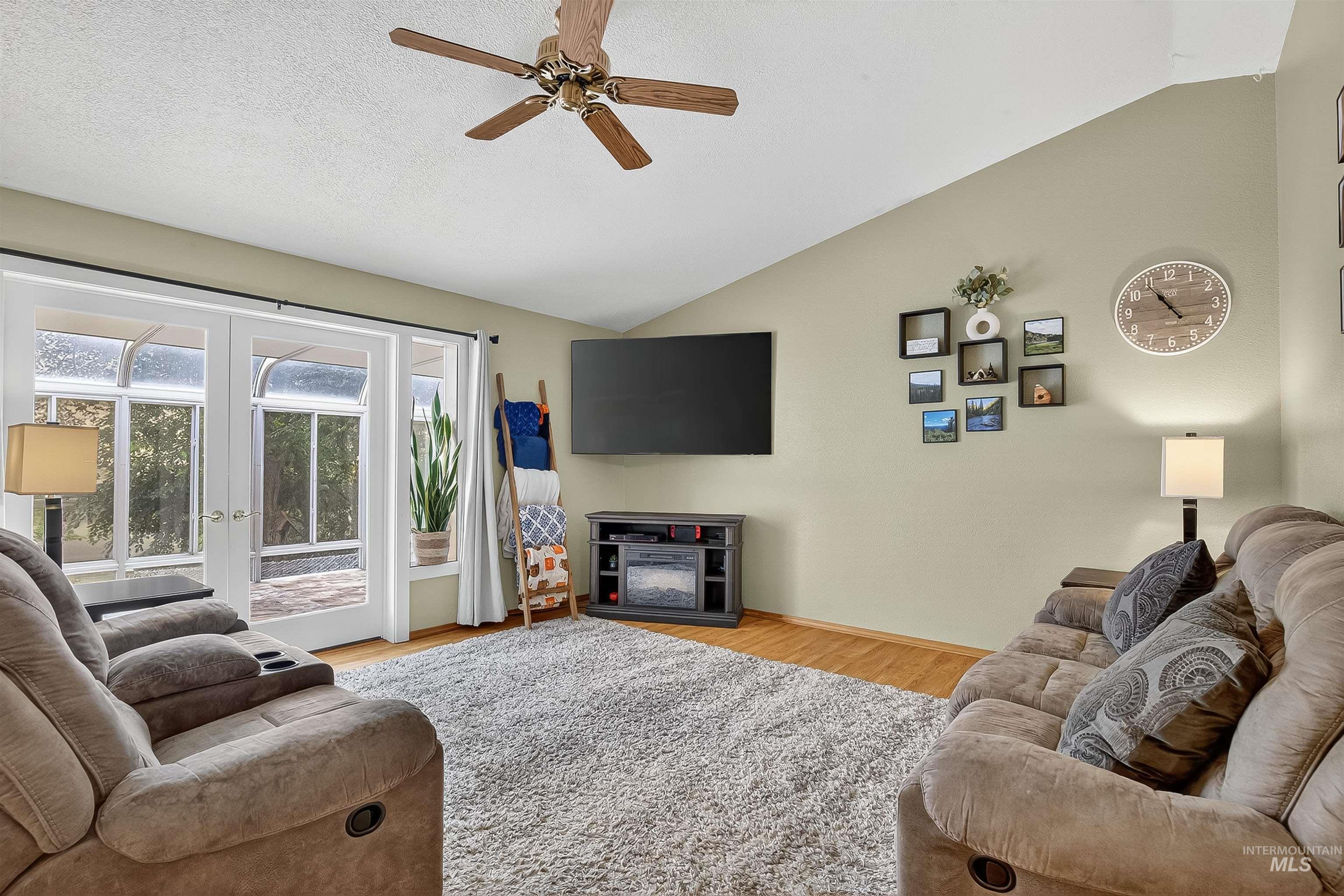 Living room featuring vaulted ceiling, light wood-type flooring, ceiling fan, and french doors