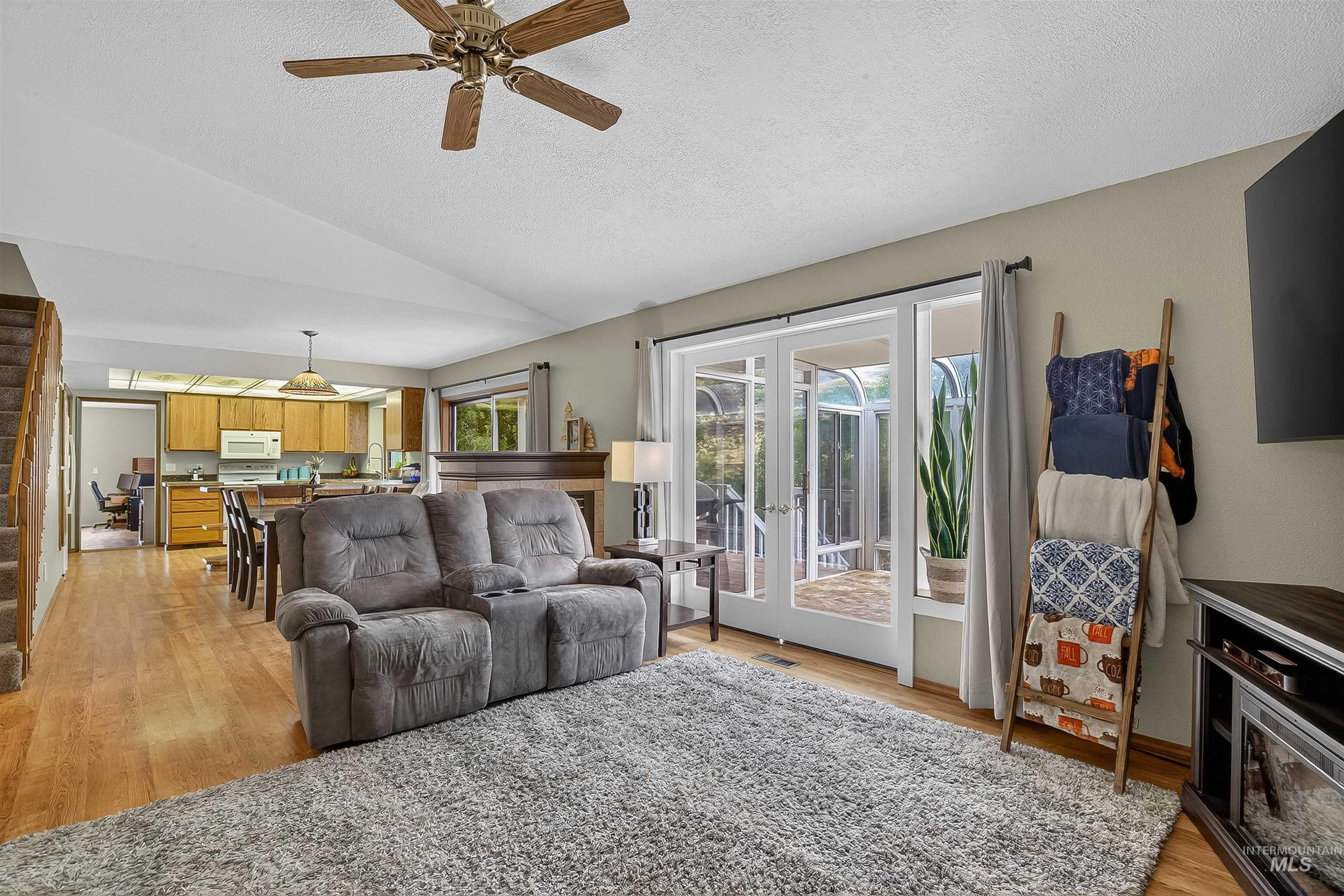 Living room featuring light wood-style flooring, a textured ceiling, vaulted ceiling, ceiling fan, and stairs