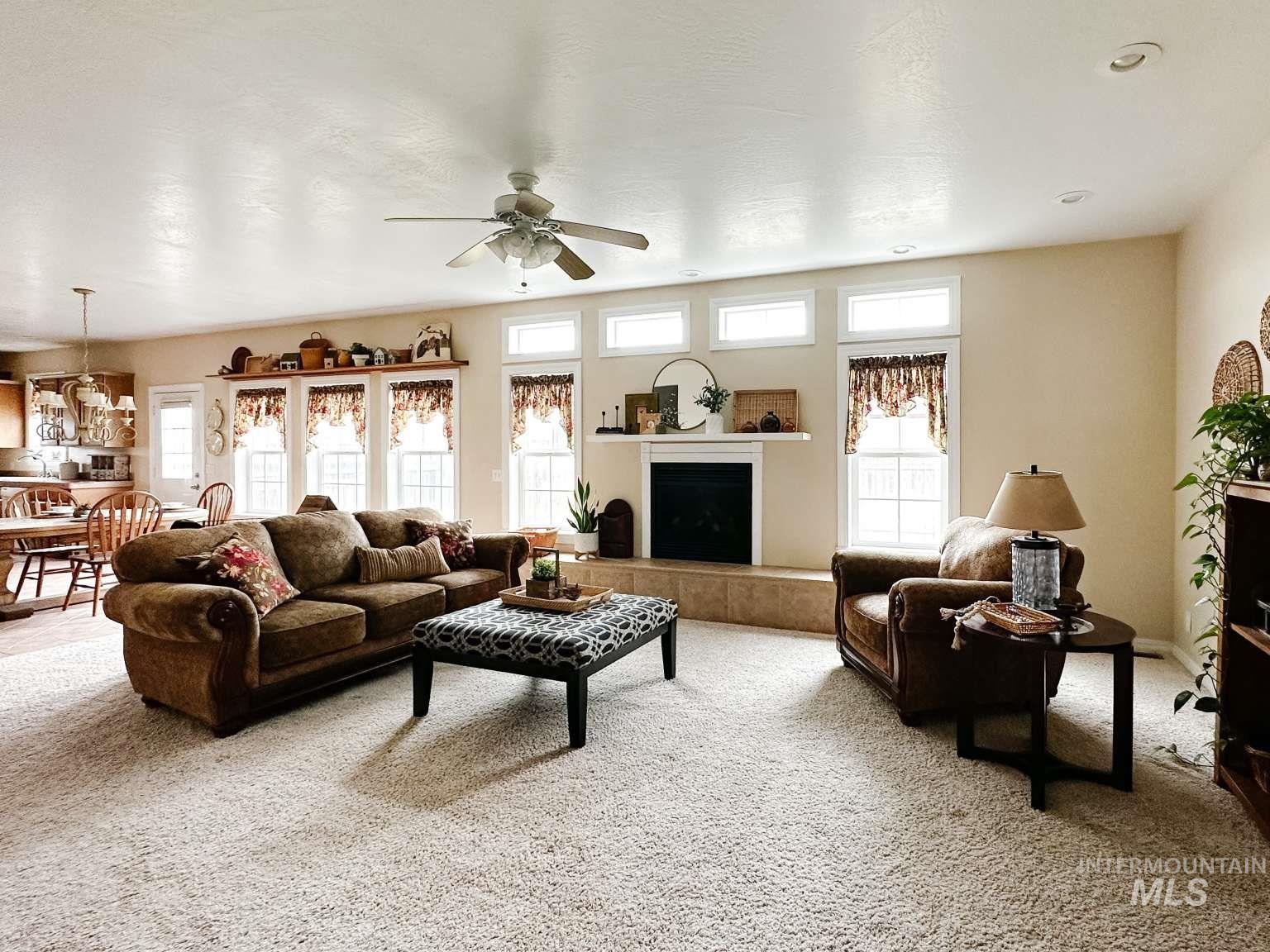 Living area featuring light colored carpet, a tiled fireplace, and a ceiling fan