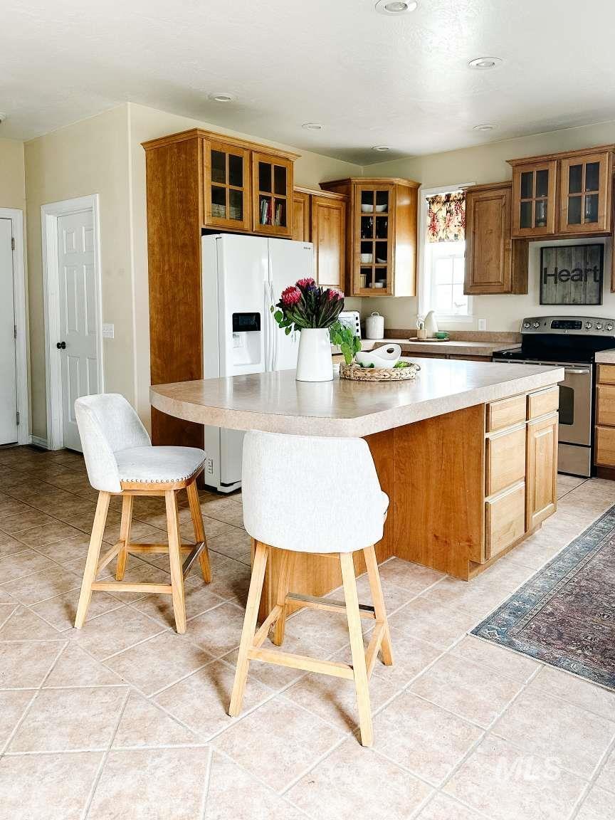 Kitchen featuring electric stove, glass insert cabinets, light tile patterned flooring, and brown cabinetry