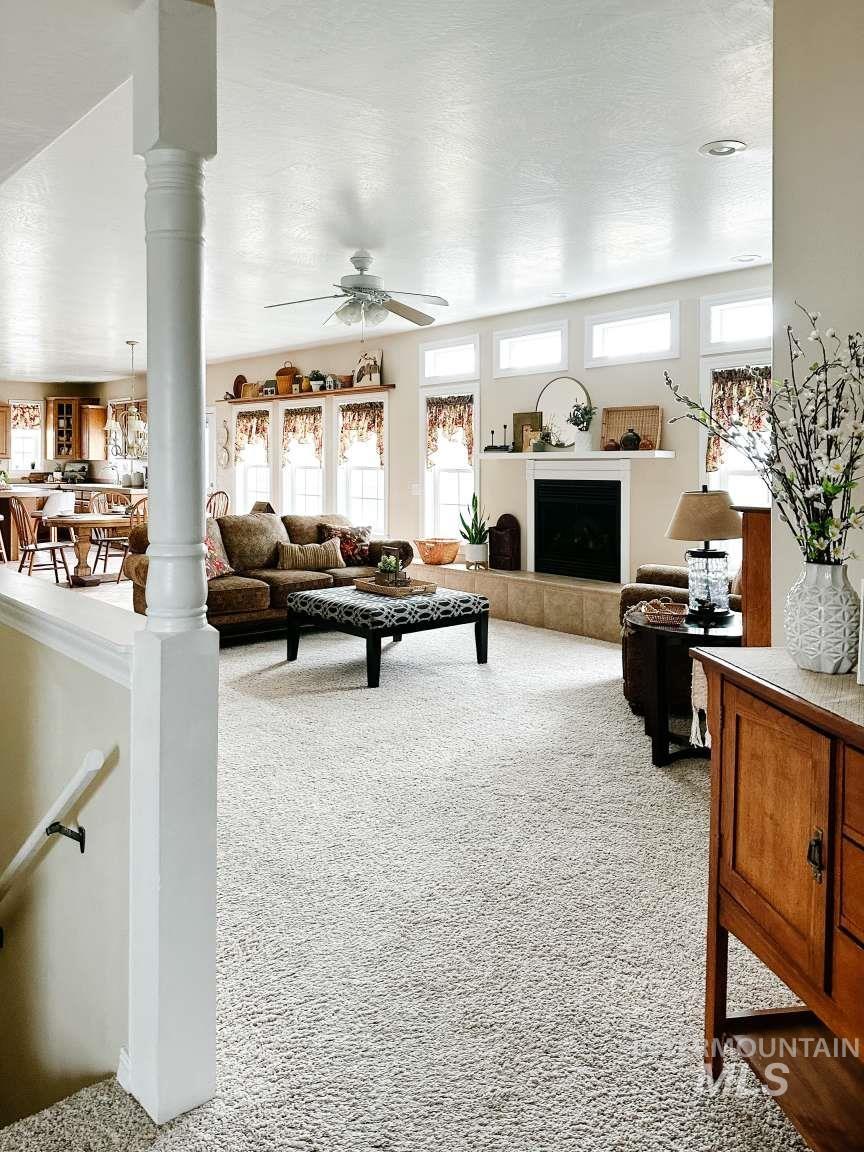 Living room featuring light carpet, a tile fireplace, ornate columns, and ceiling fan