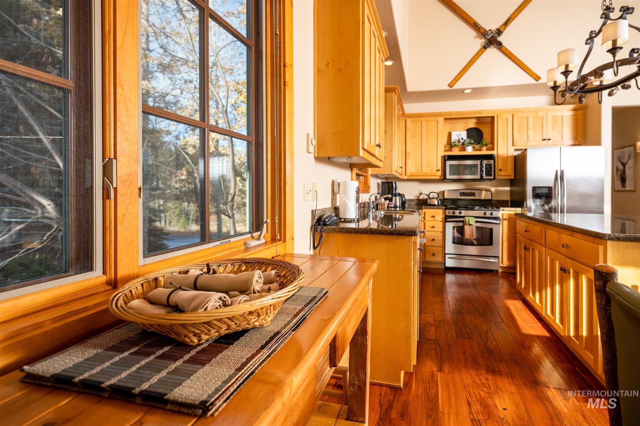 Kitchen featuring stainless steel appliances, dark stone countertops, a chandelier, dark wood finished floors, and open shelves