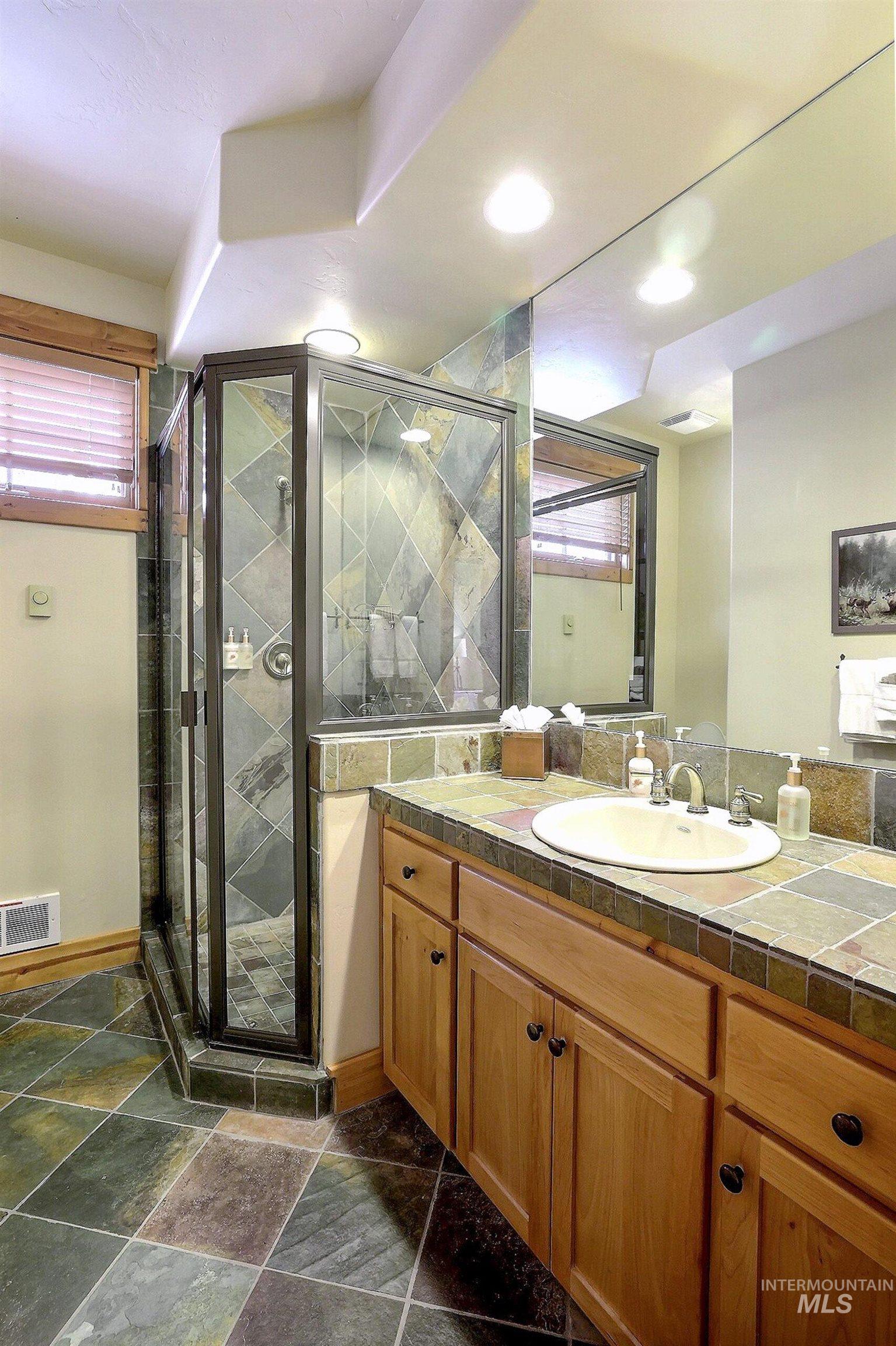 Full bath featuring vanity, a shower stall, and stone tile floors