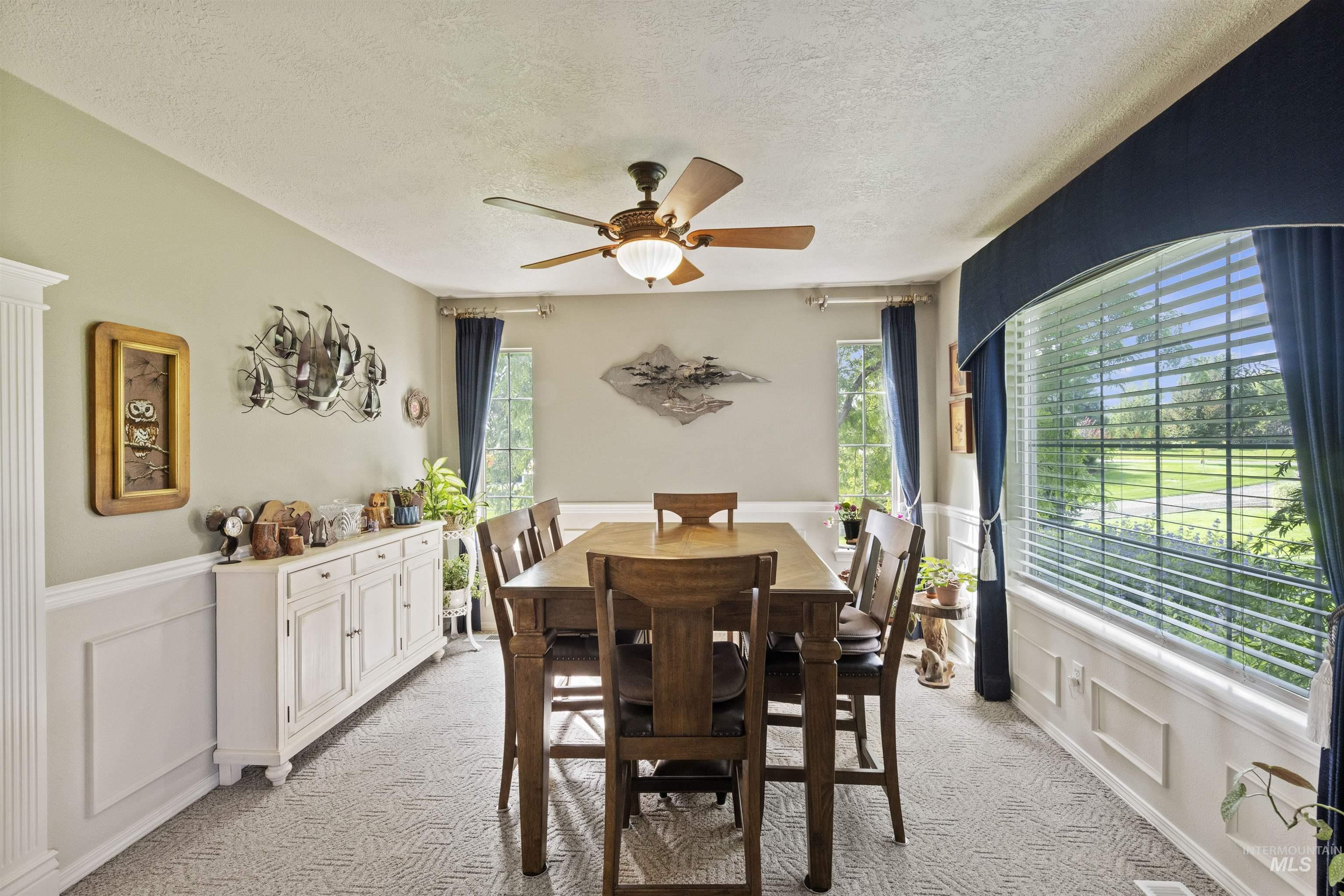 Dining area with a decorative wall, a wainscoted wall, light colored carpet, a textured ceiling, and ceiling fan