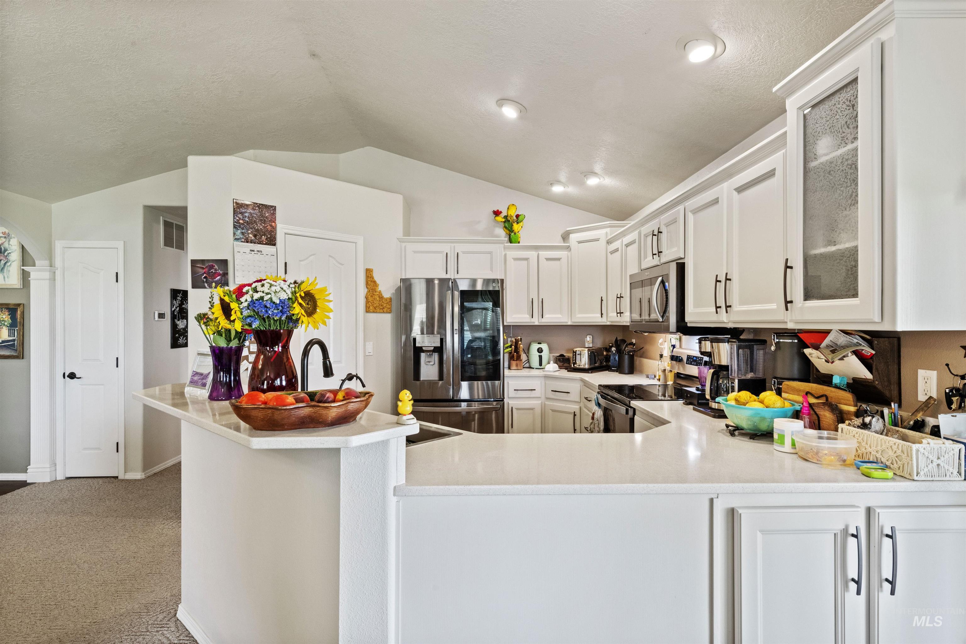 Kitchen with appliances with stainless steel finishes, white cabinetry, glass insert cabinets, lofted ceiling, and light colored carpet