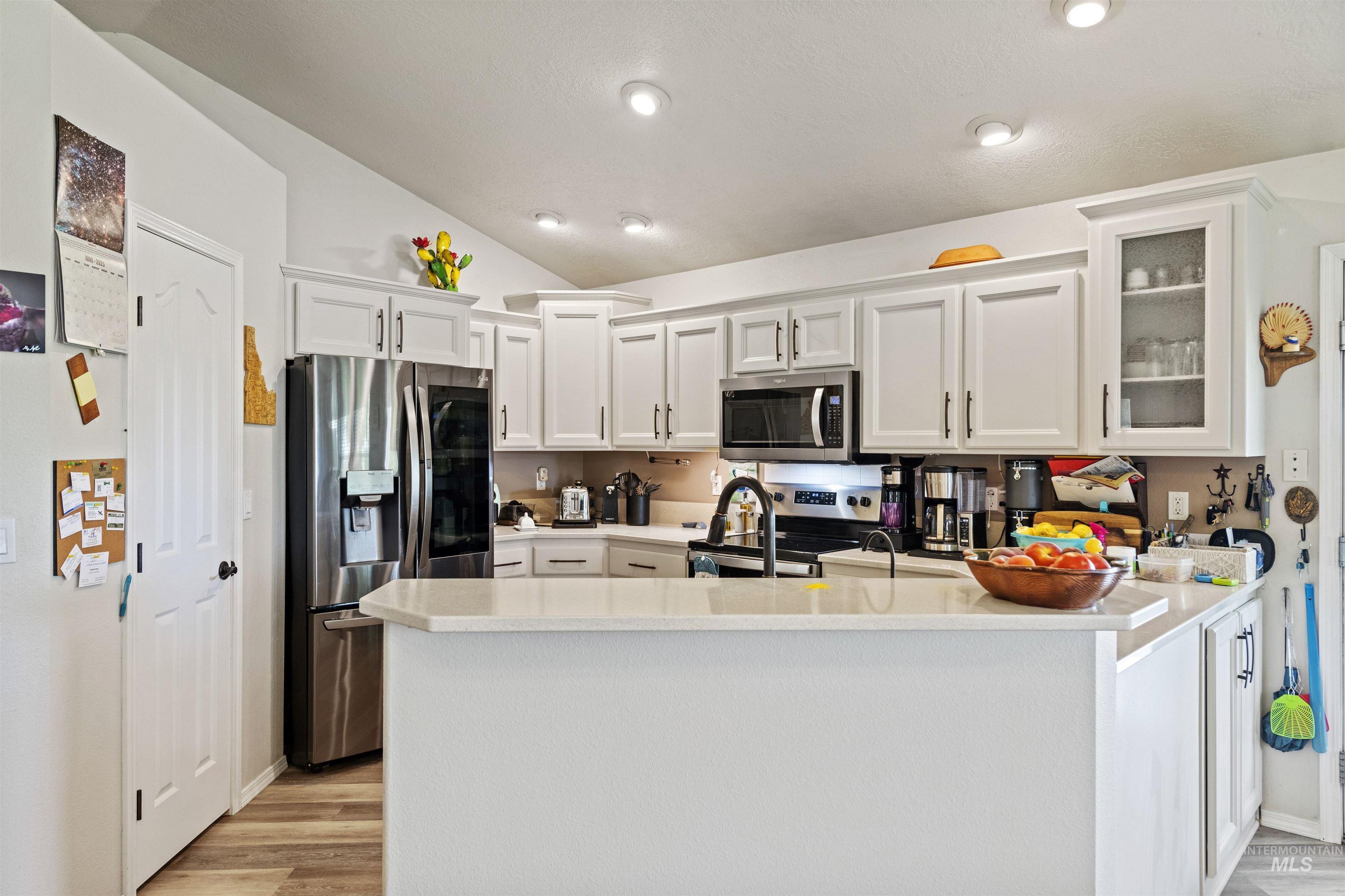 Kitchen with white cabinets, appliances with stainless steel finishes, a peninsula, light wood-style floors, and glass insert cabinets