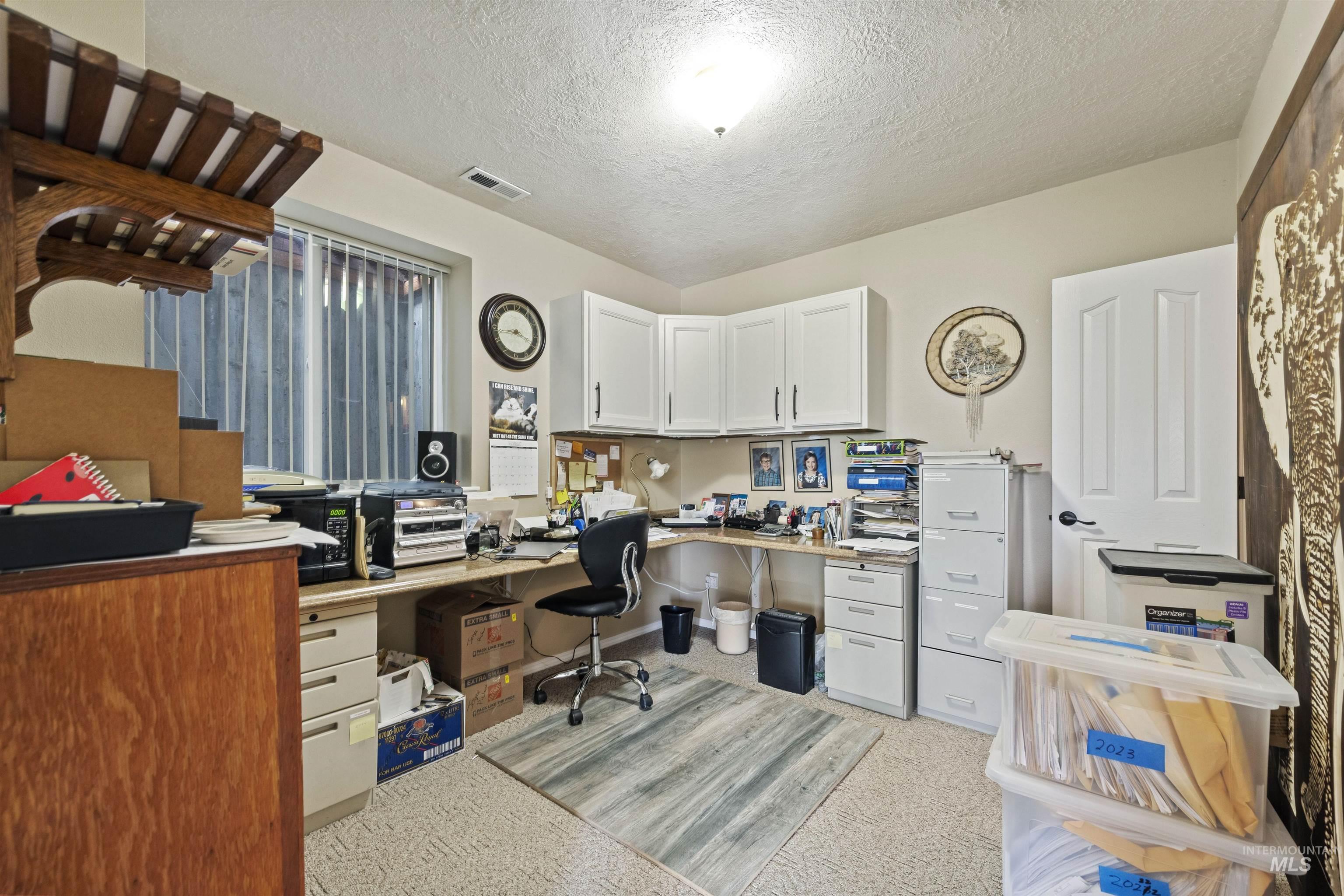 Office area with a textured ceiling, built in study area, and light colored carpet