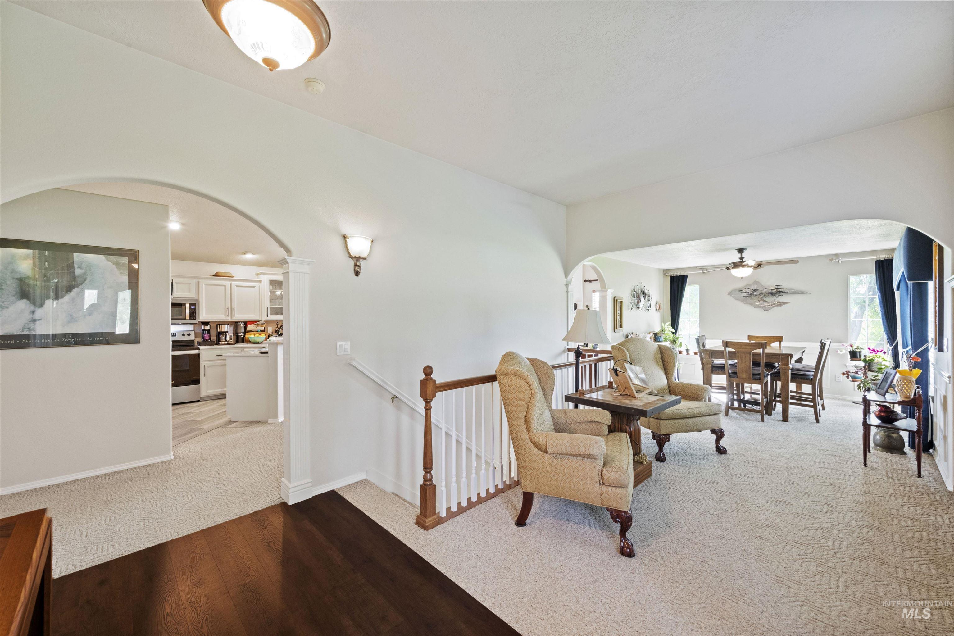 Sitting room with arched walkways, light colored carpet, ceiling fan, and an upstairs landing