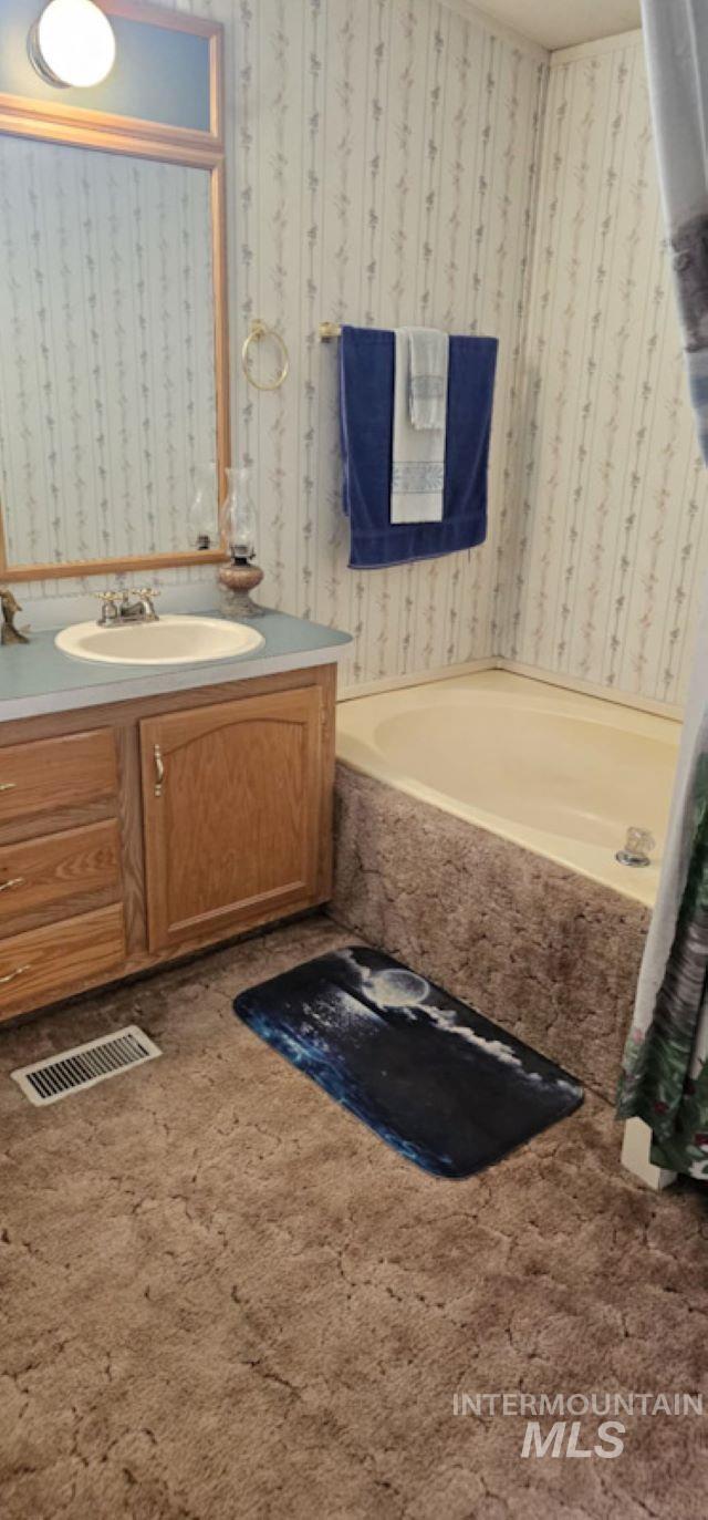 Bathroom with wallpapered walls, a bath, and vanity