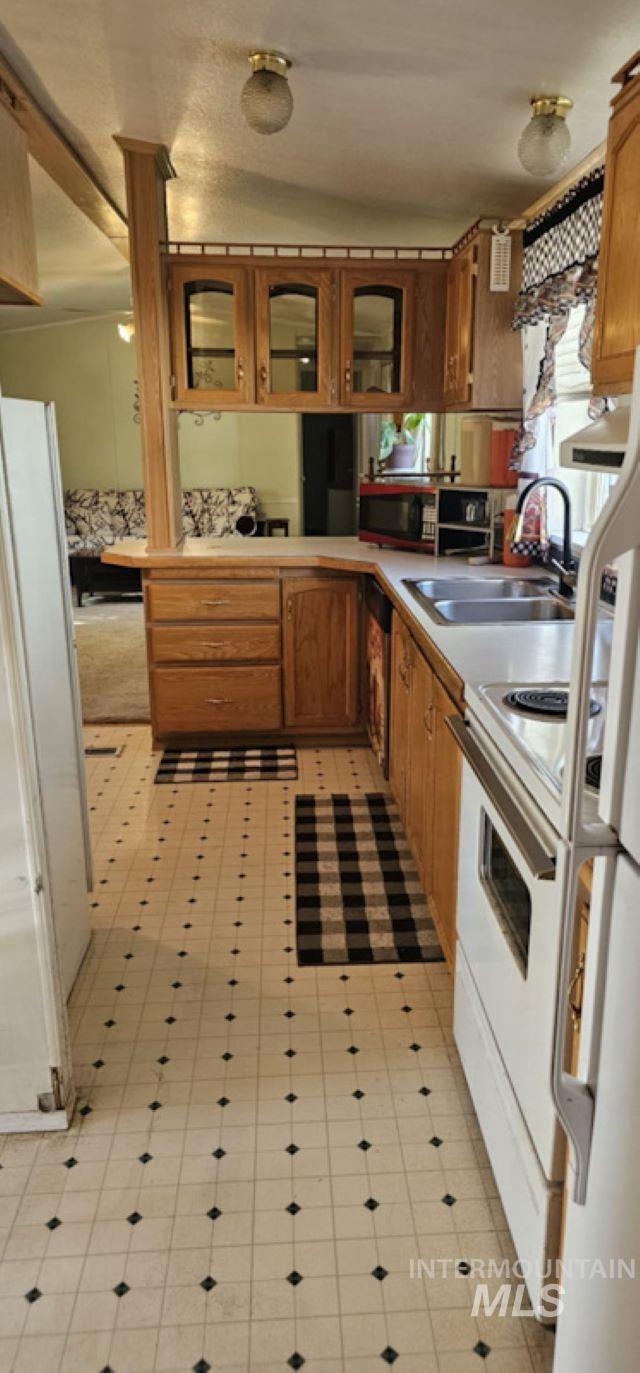 Kitchen featuring light countertops, glass insert cabinets, white appliances, and brown cabinetry