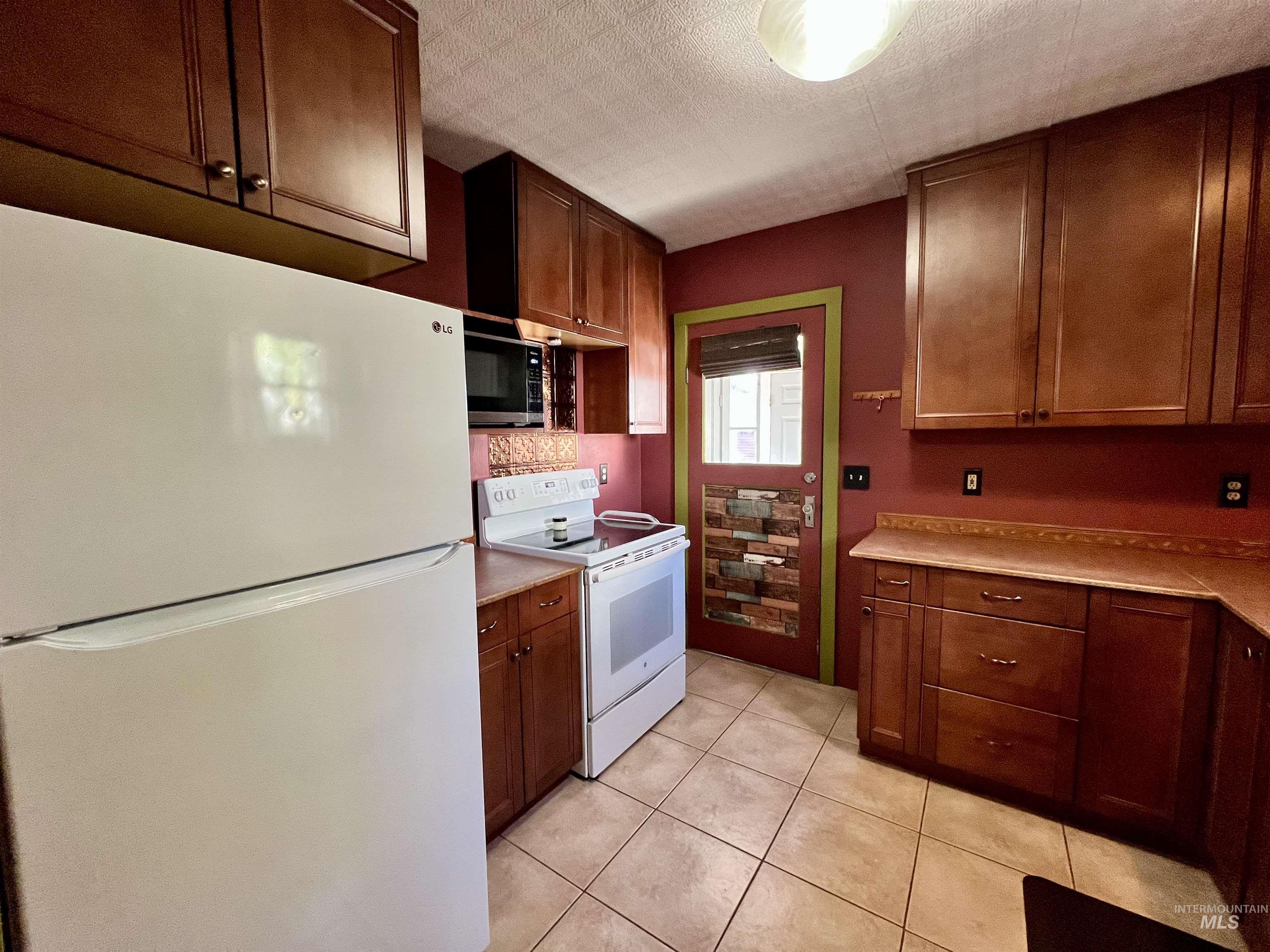Kitchen with white appliances, light countertops, light tile patterned flooring, and a textured ceiling