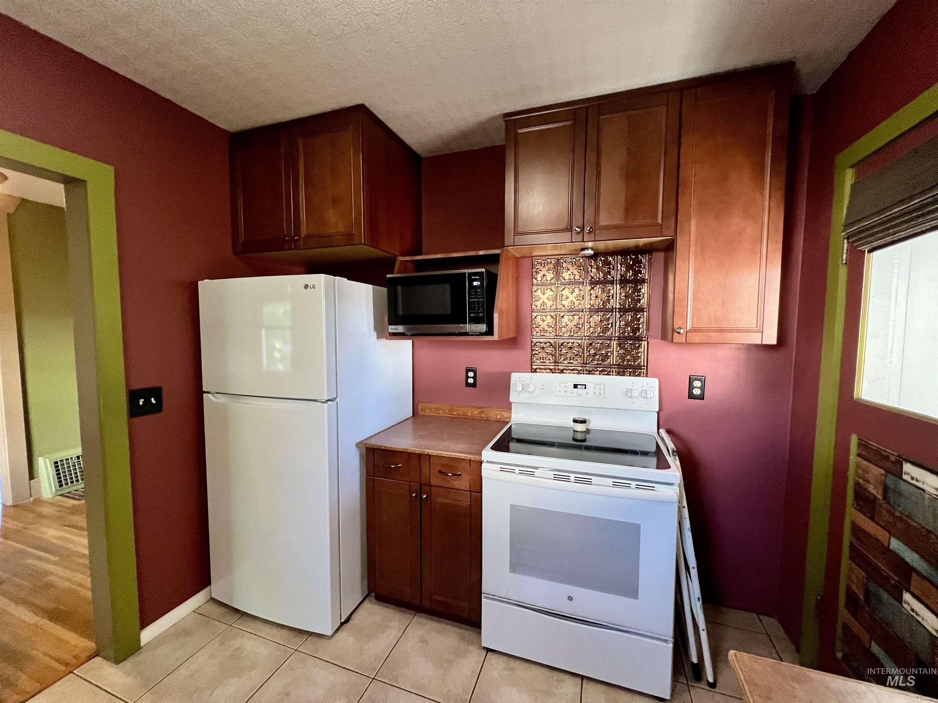 Kitchen with white appliances, light tile patterned floors, light countertops, and a textured ceiling