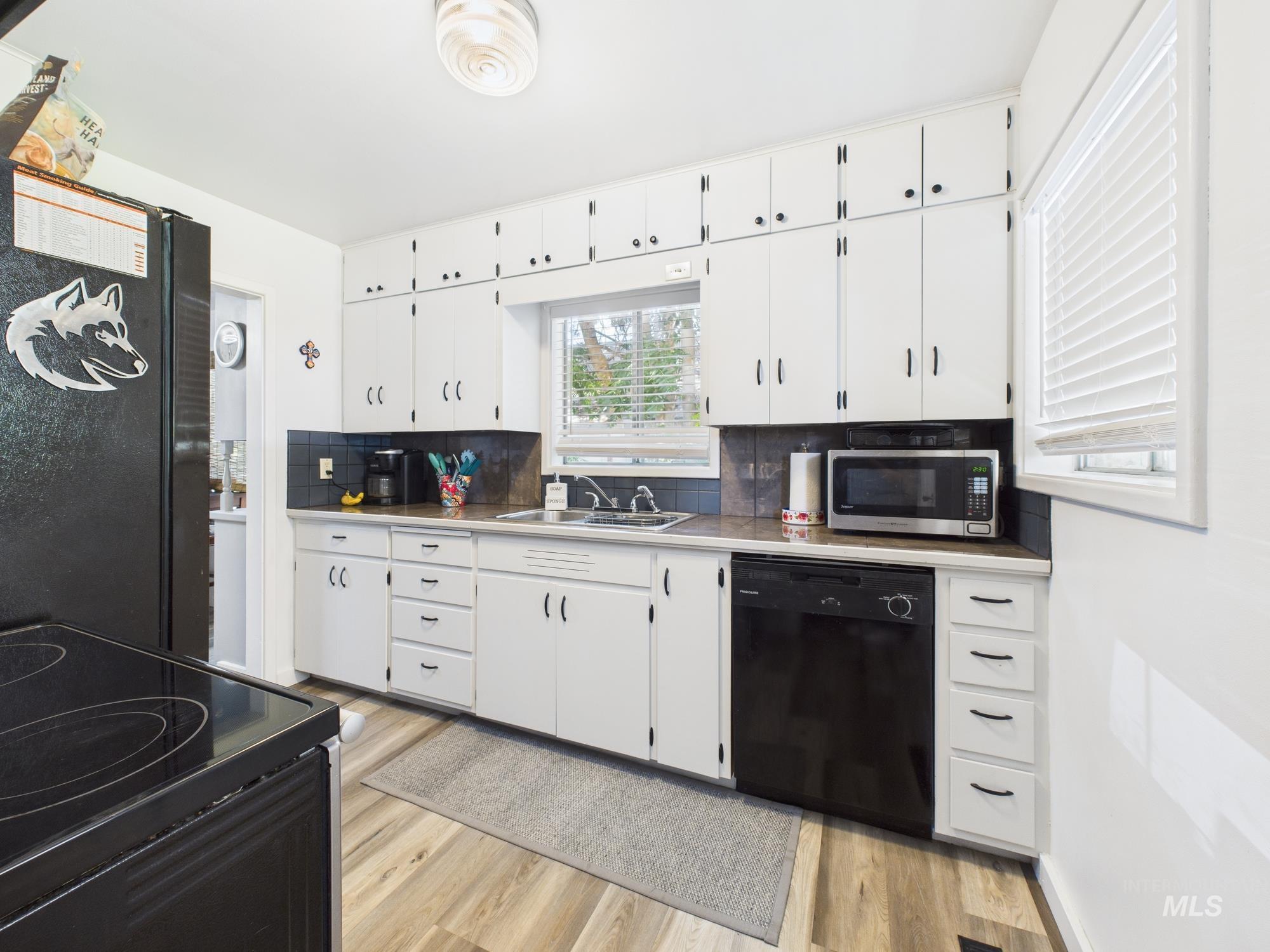 Kitchen with white cabinets, tasteful backsplash, black appliances, and light wood-type flooring