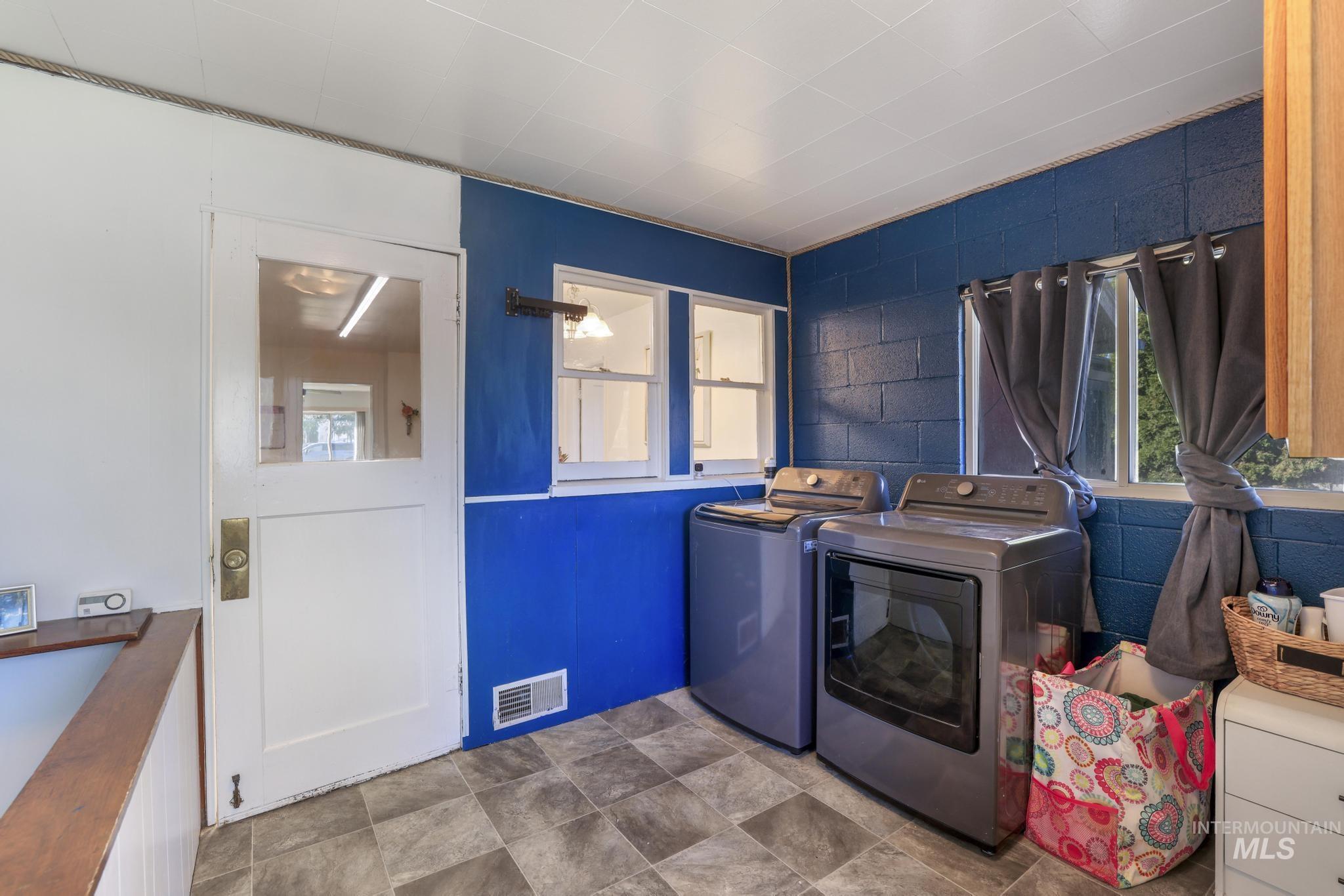 Laundry area with concrete block wall, washer and clothes dryer, healthy amount of natural light, and stone finish floors