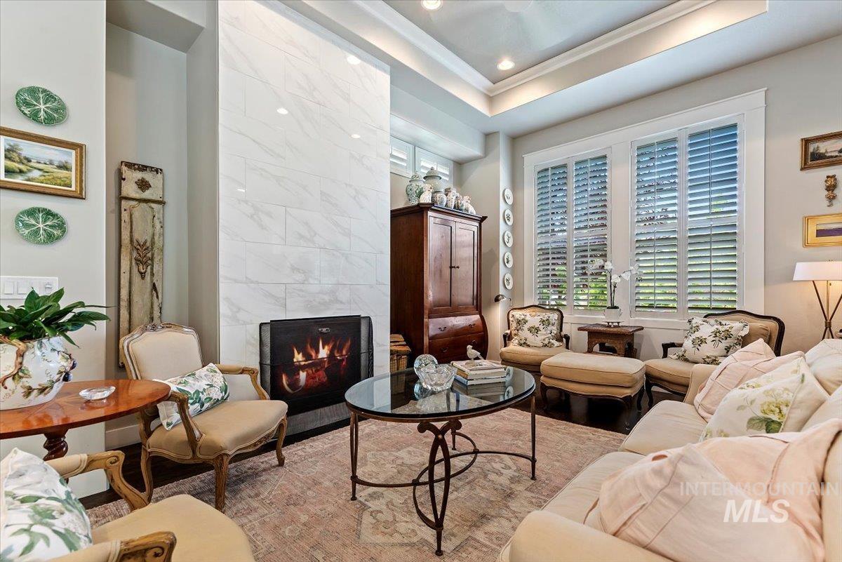 Living area with a tile fireplace, a raised ceiling, wood finished floors, crown molding, and recessed lighting