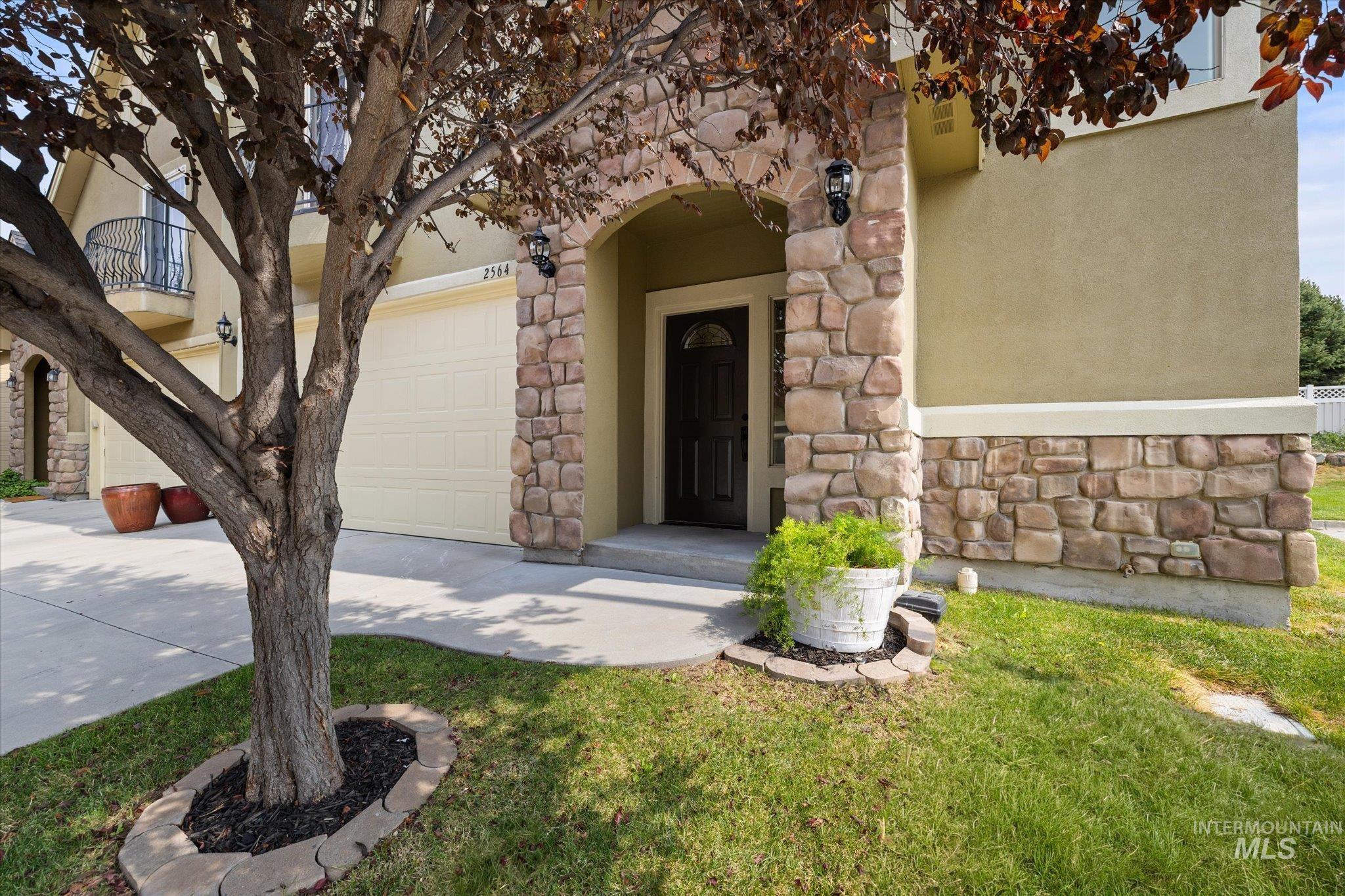View of exterior entry with stone siding, concrete driveway, a garage, and a yard