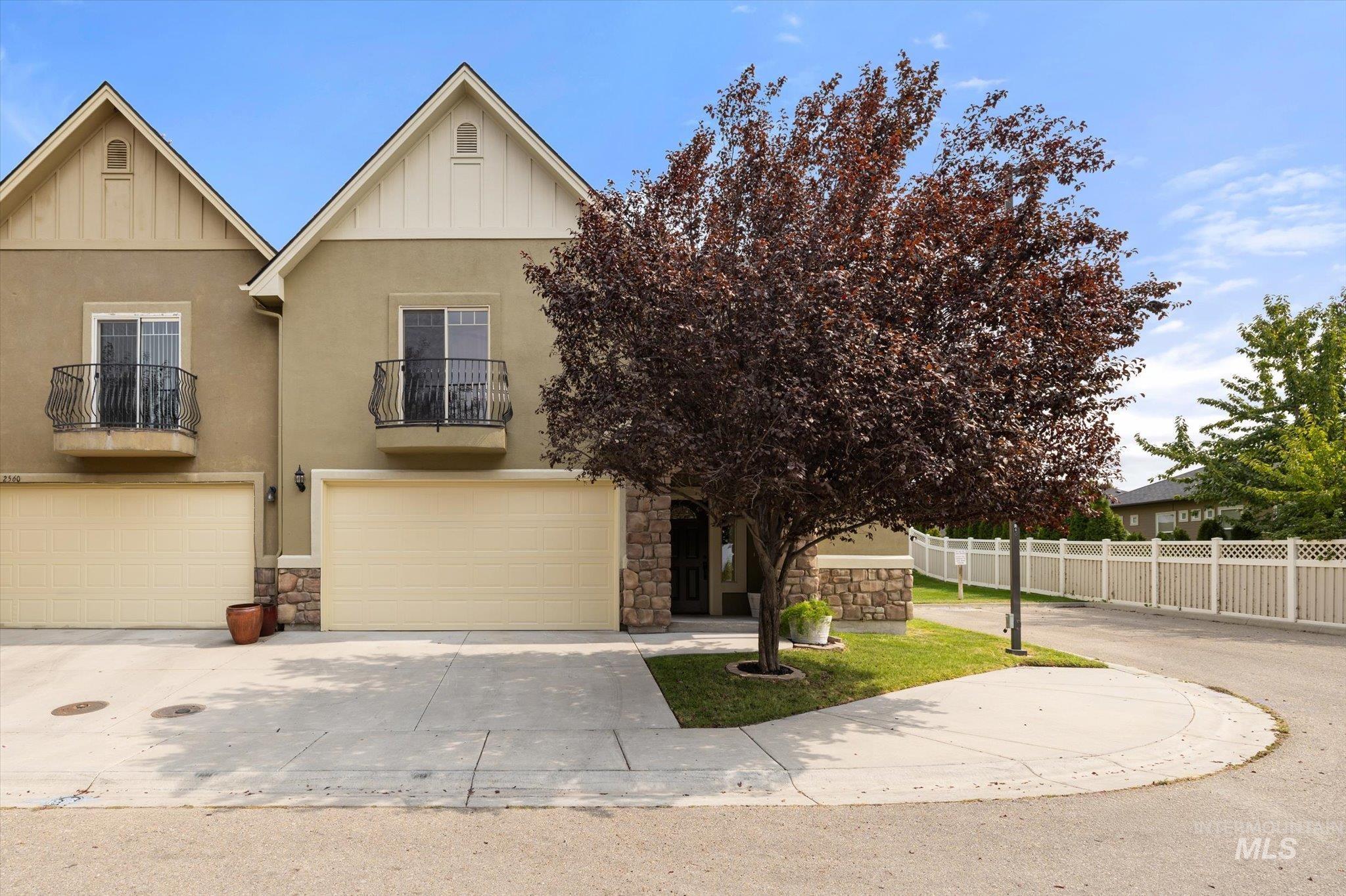 View of front facade featuring a balcony, stone siding, driveway, an attached garage, and stucco siding