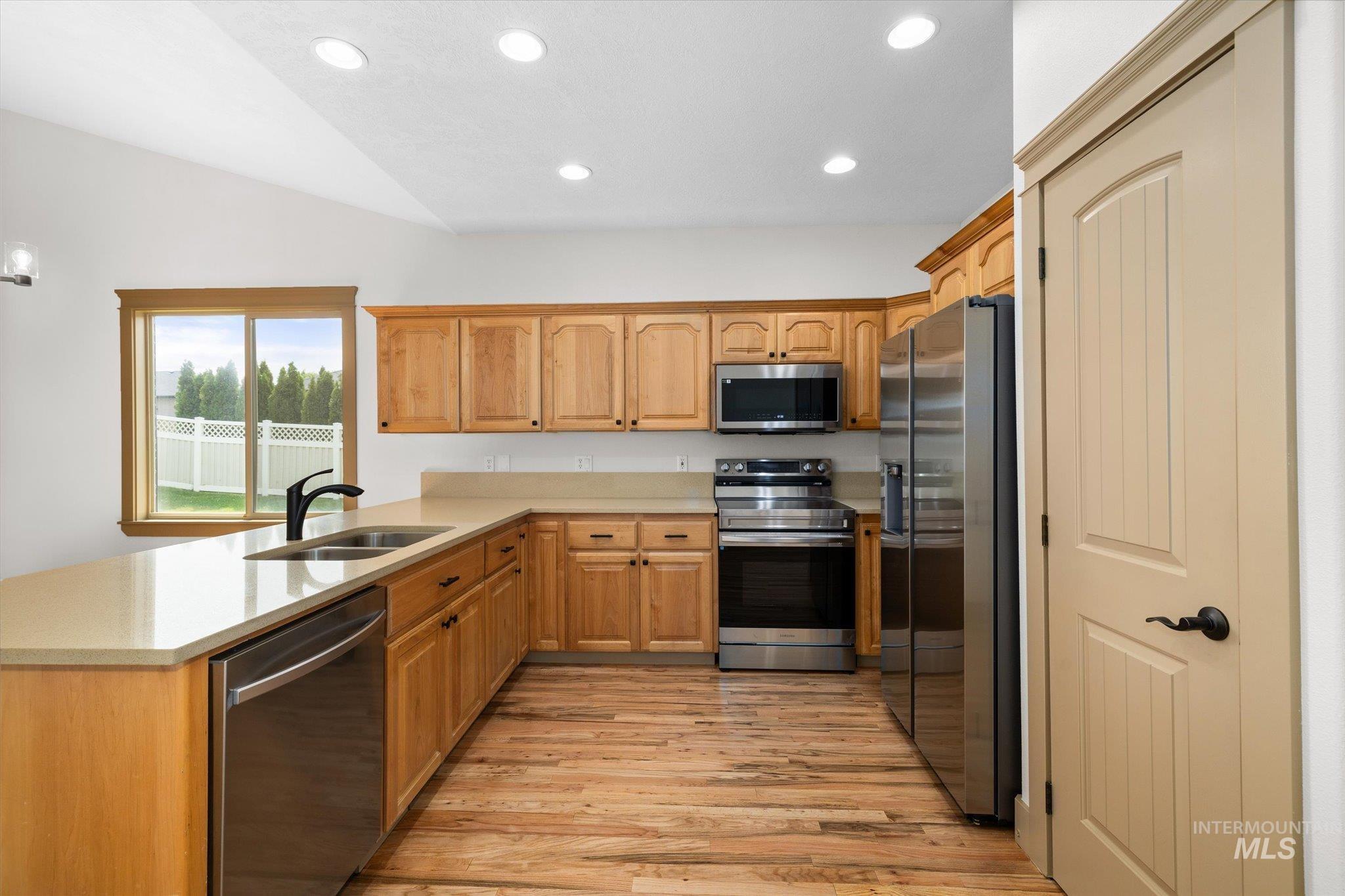 Kitchen featuring stainless steel appliances, recessed lighting, light wood-style floors, a peninsula, and vaulted ceiling