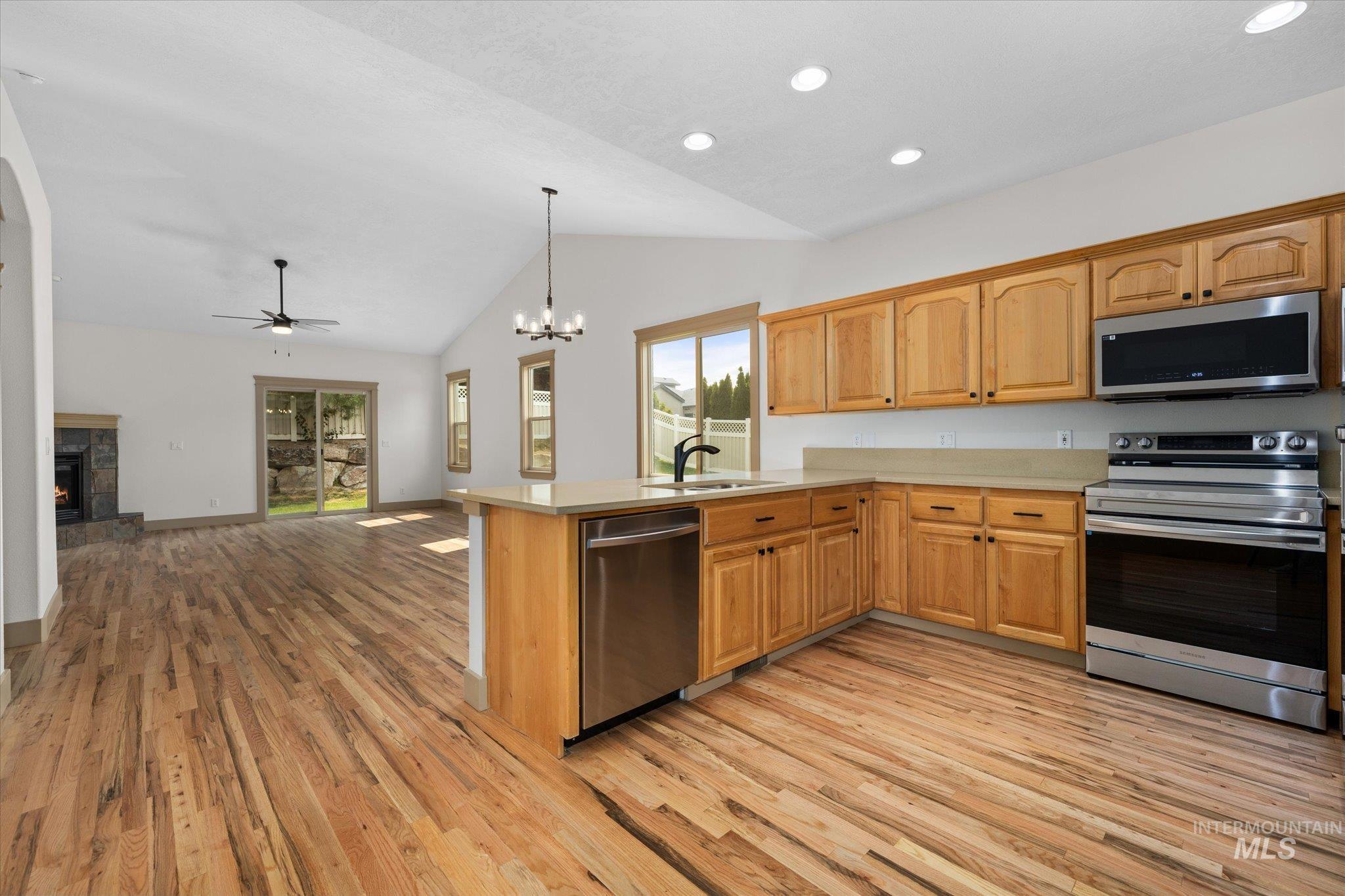 Kitchen with a chandelier, appliances with stainless steel finishes, light countertops, a stone fireplace, and decorative light fixtures
