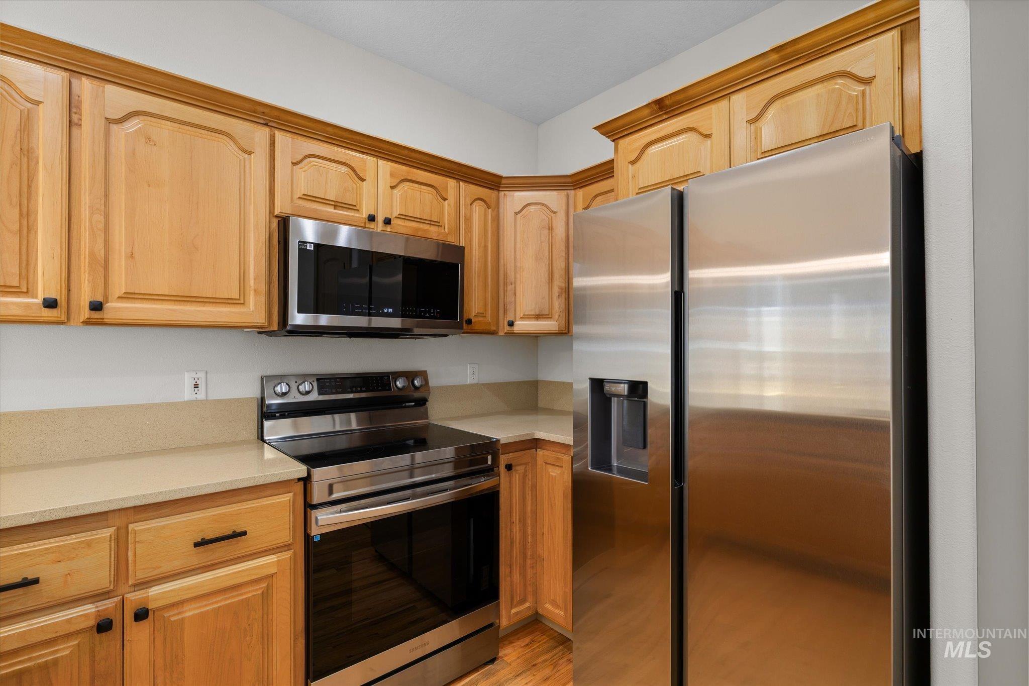 Kitchen featuring appliances with stainless steel finishes, light wood-style flooring, light brown cabinetry, and light stone counters