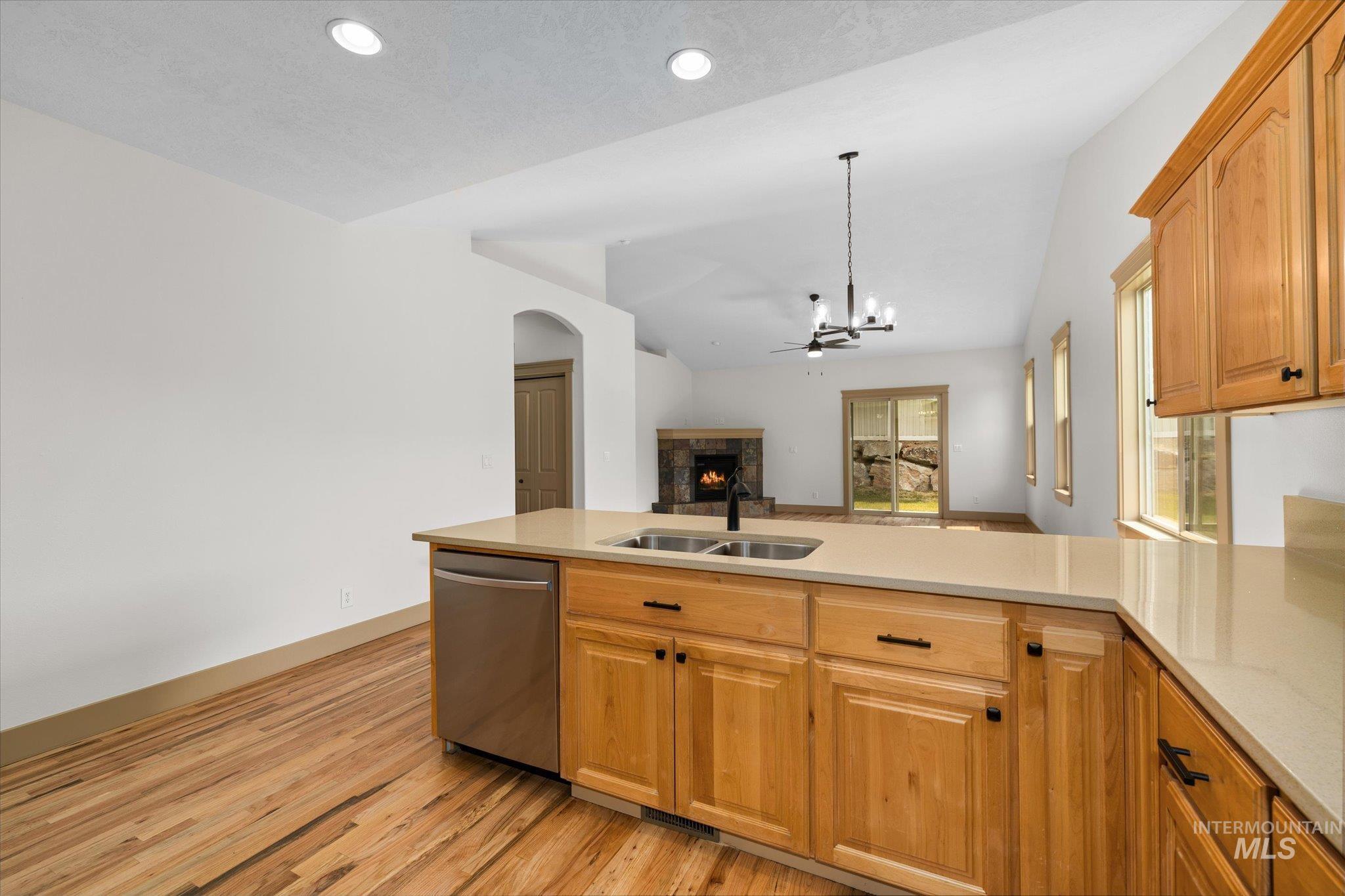 Kitchen featuring open floor plan, stainless steel dishwasher, light wood-style flooring, a peninsula, and a fireplace