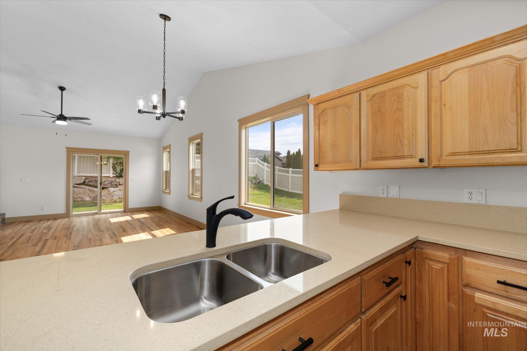 Kitchen featuring light wood-type flooring, vaulted ceiling, pendant lighting, a chandelier, and light stone counters