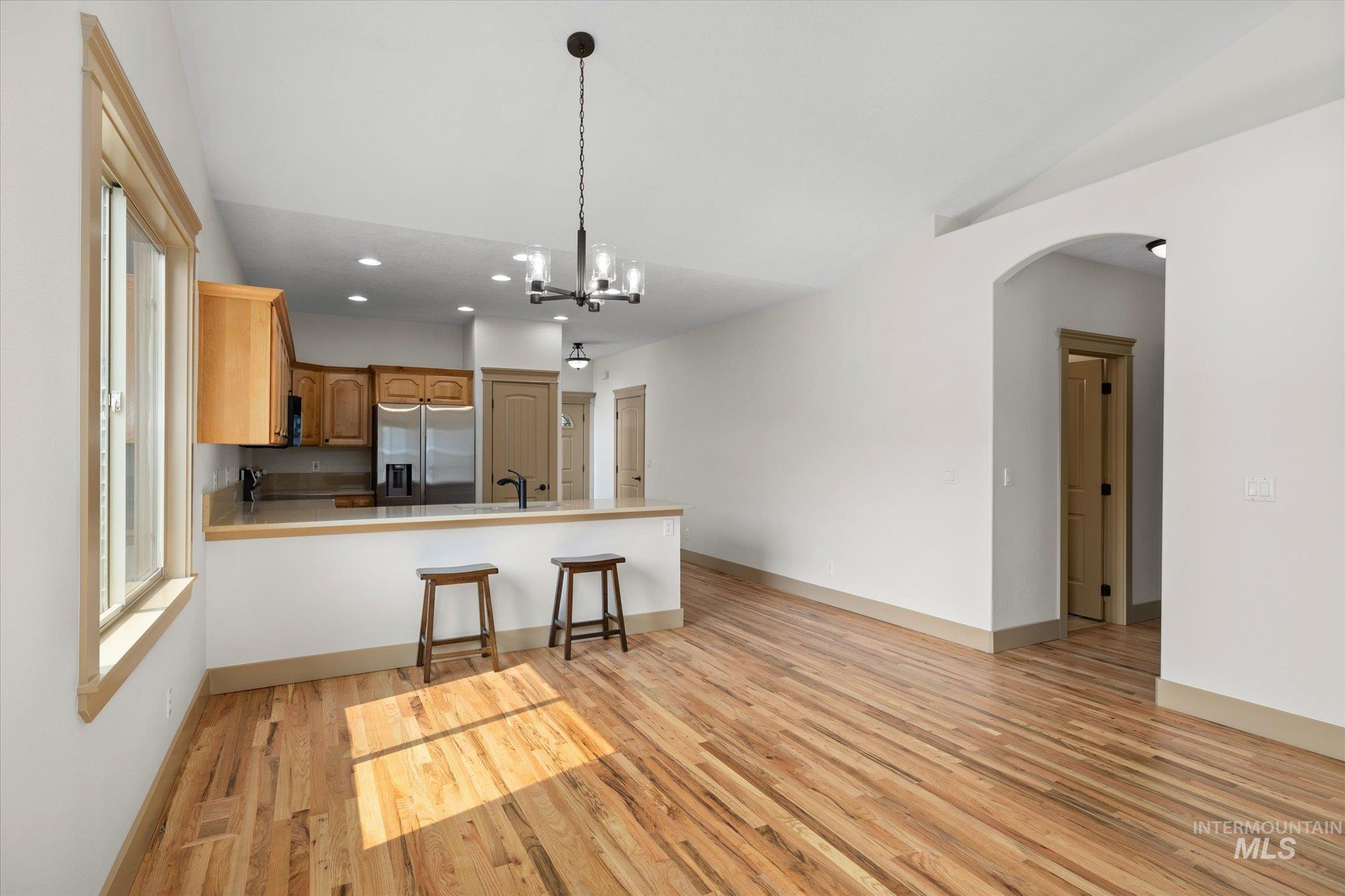 Kitchen with a kitchen bar, light wood-style floors, stainless steel fridge with ice dispenser, hanging light fixtures, and light countertops