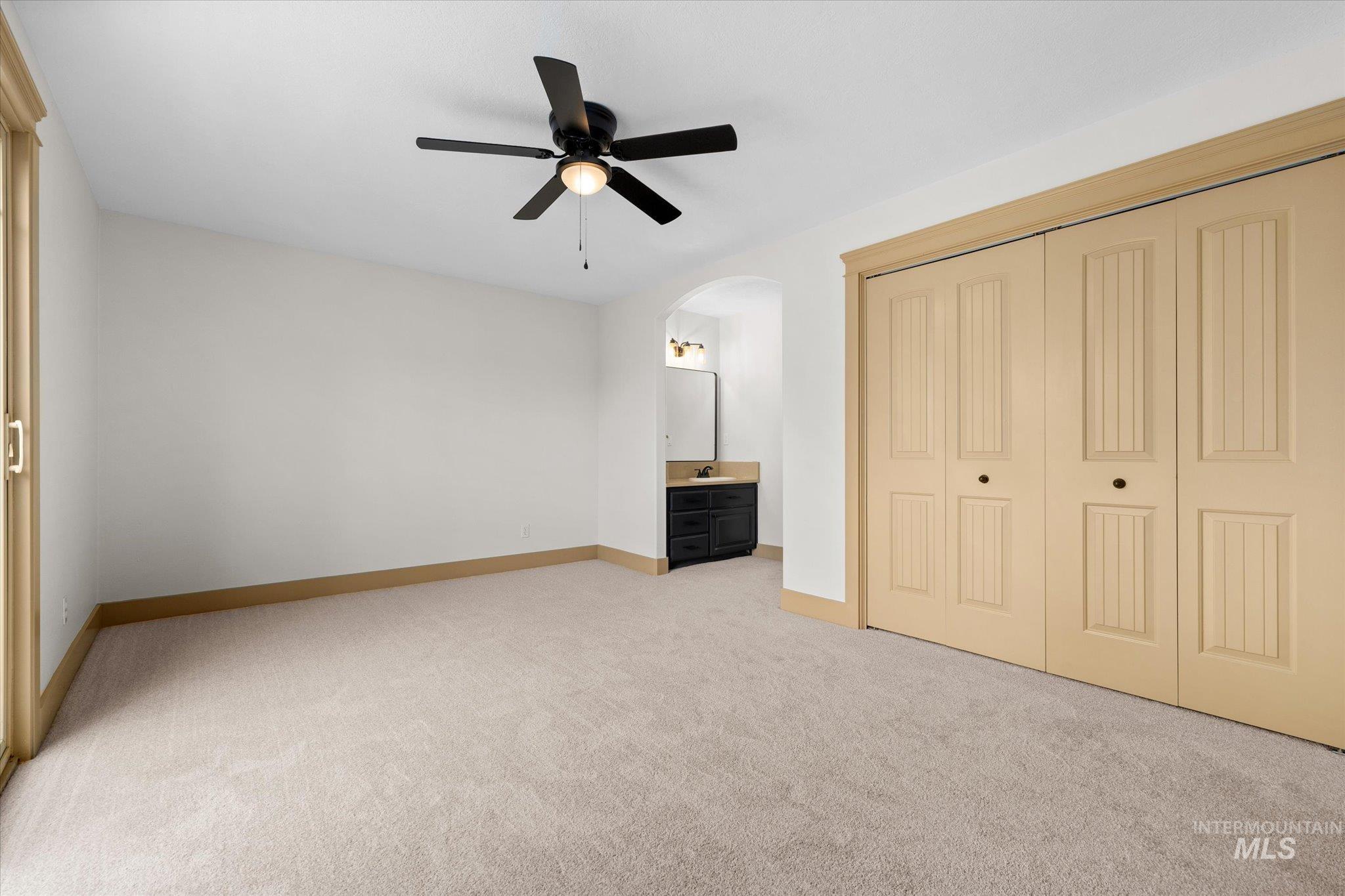Unfurnished bedroom featuring light colored carpet, arched walkways, connected bathroom, a ceiling fan, and a closet