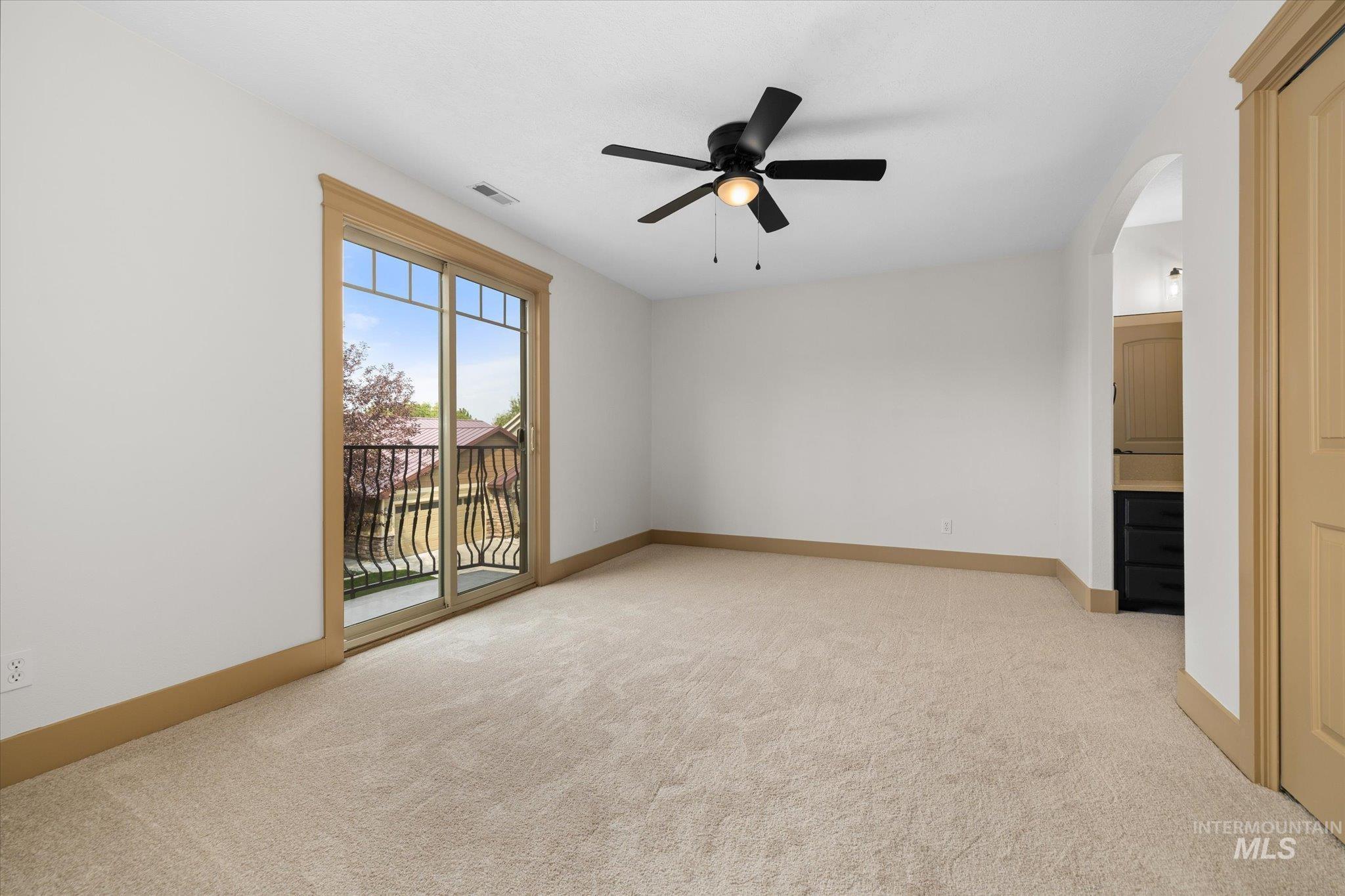 Empty room with light carpet, arched walkways, and ceiling fan