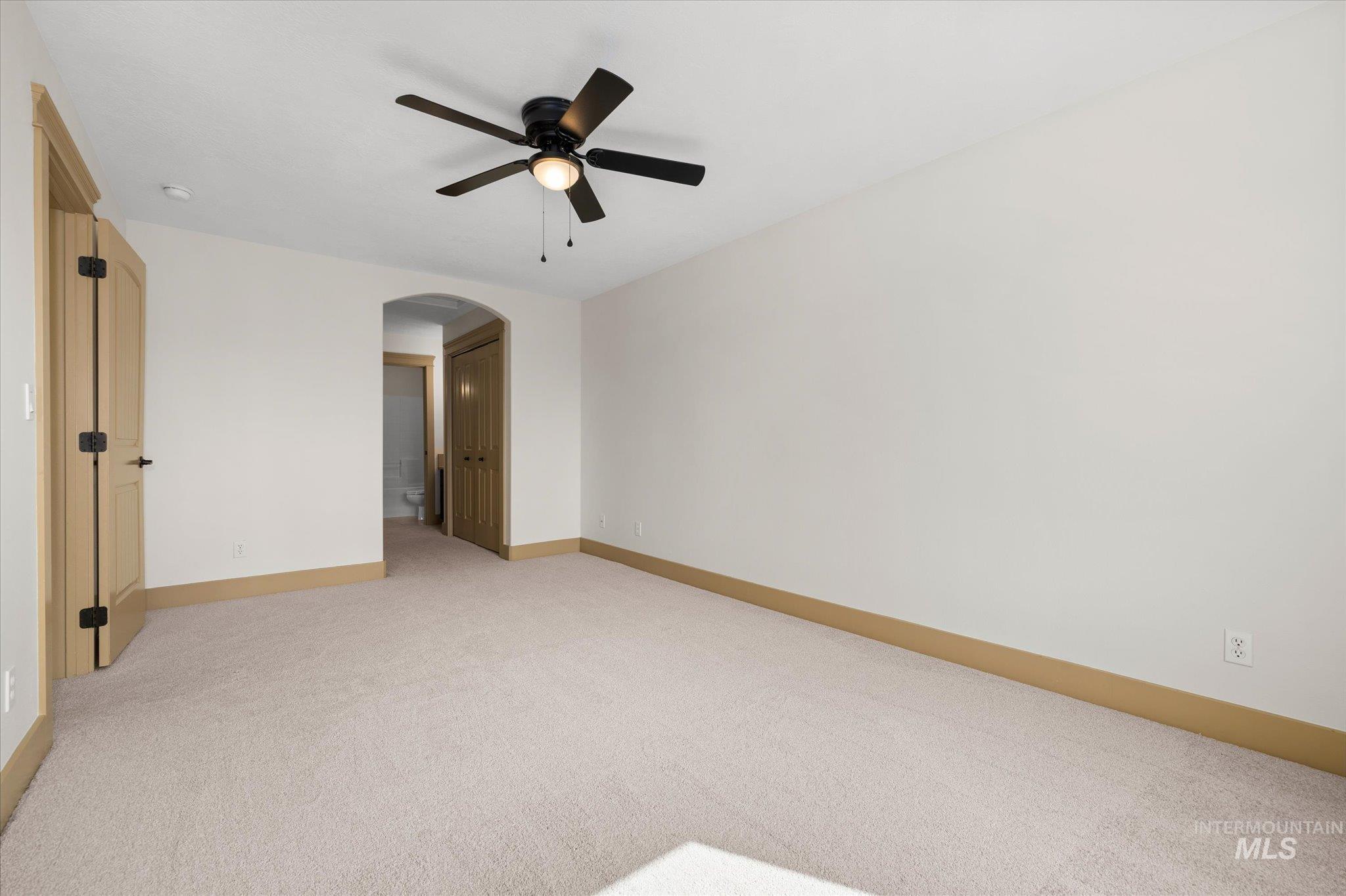 Spare room featuring light colored carpet, arched walkways, and ceiling fan