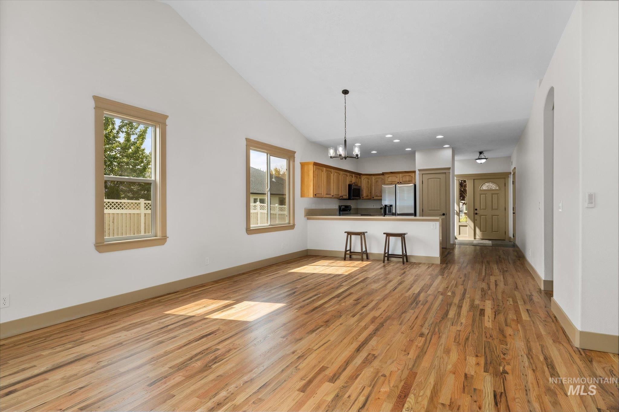 Unfurnished living room featuring a chandelier, light wood finished floors, high vaulted ceiling, and recessed lighting