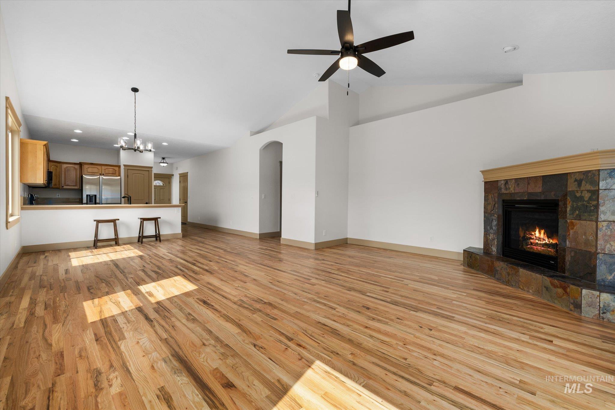 Unfurnished living room featuring a chandelier, light wood-style floors, a tile fireplace, recessed lighting, and high vaulted ceiling