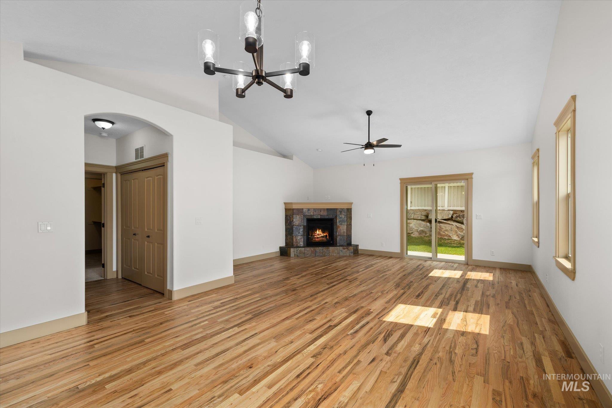 Unfurnished living room featuring lofted ceiling, light wood-style floors, a stone fireplace, ceiling fan, and arched walkways