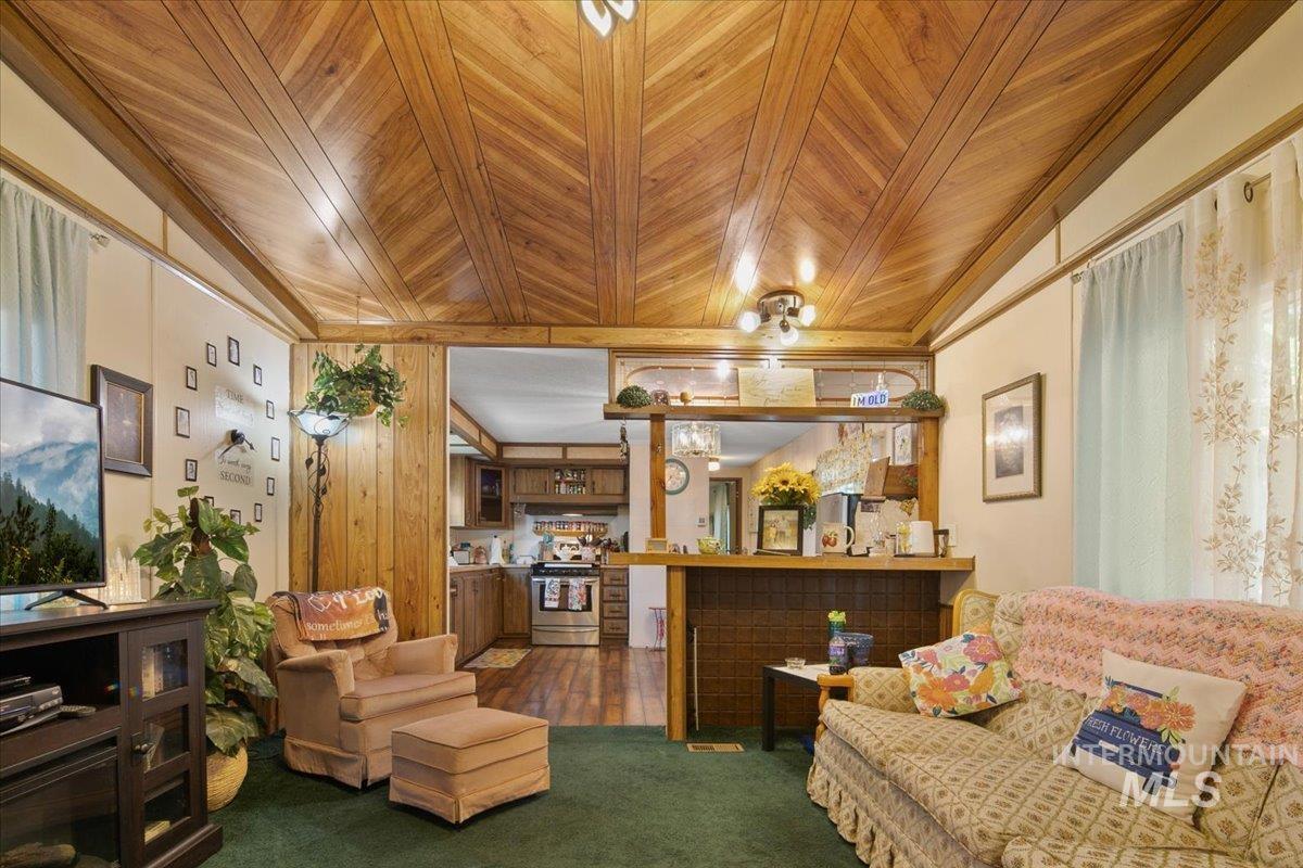 Living area with wood ceiling, dark colored carpet, and wooden walls