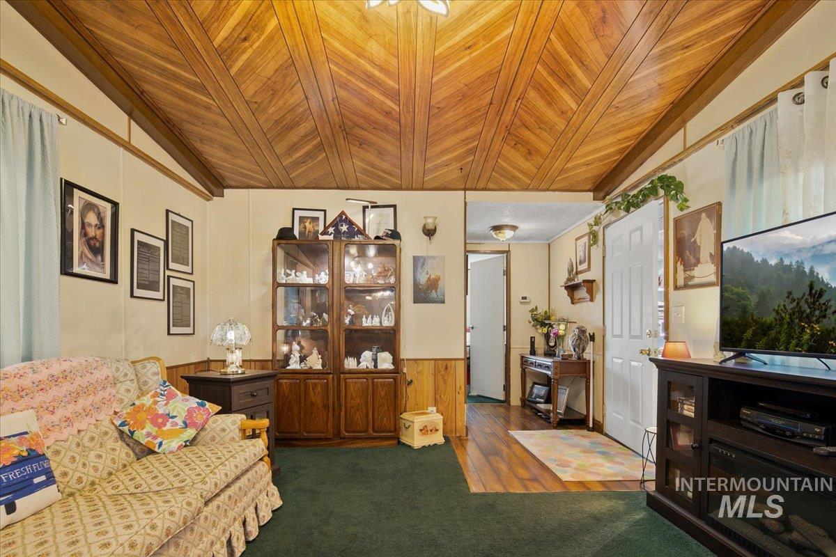 Sitting room featuring vaulted ceiling, wood walls, wood ceiling, a wainscoted wall, and dark colored carpet