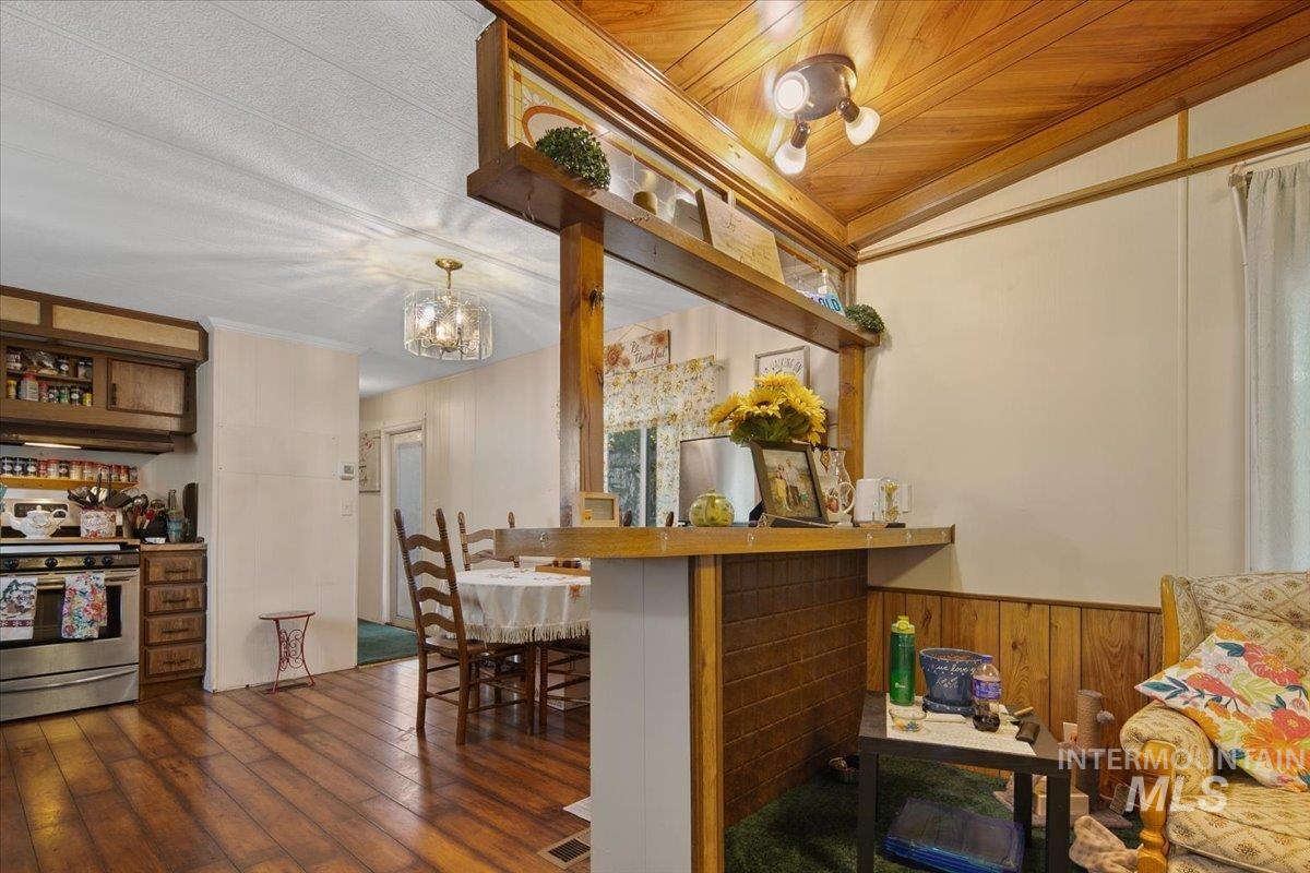 Kitchen with wooden walls, stainless steel stove, a breakfast bar area, dark wood finished floors, and vaulted ceiling