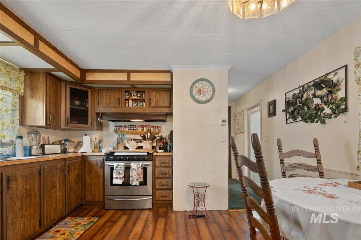 Kitchen with light countertops, stainless steel range with electric stovetop, dark wood-style flooring, brown cabinets, and range hood